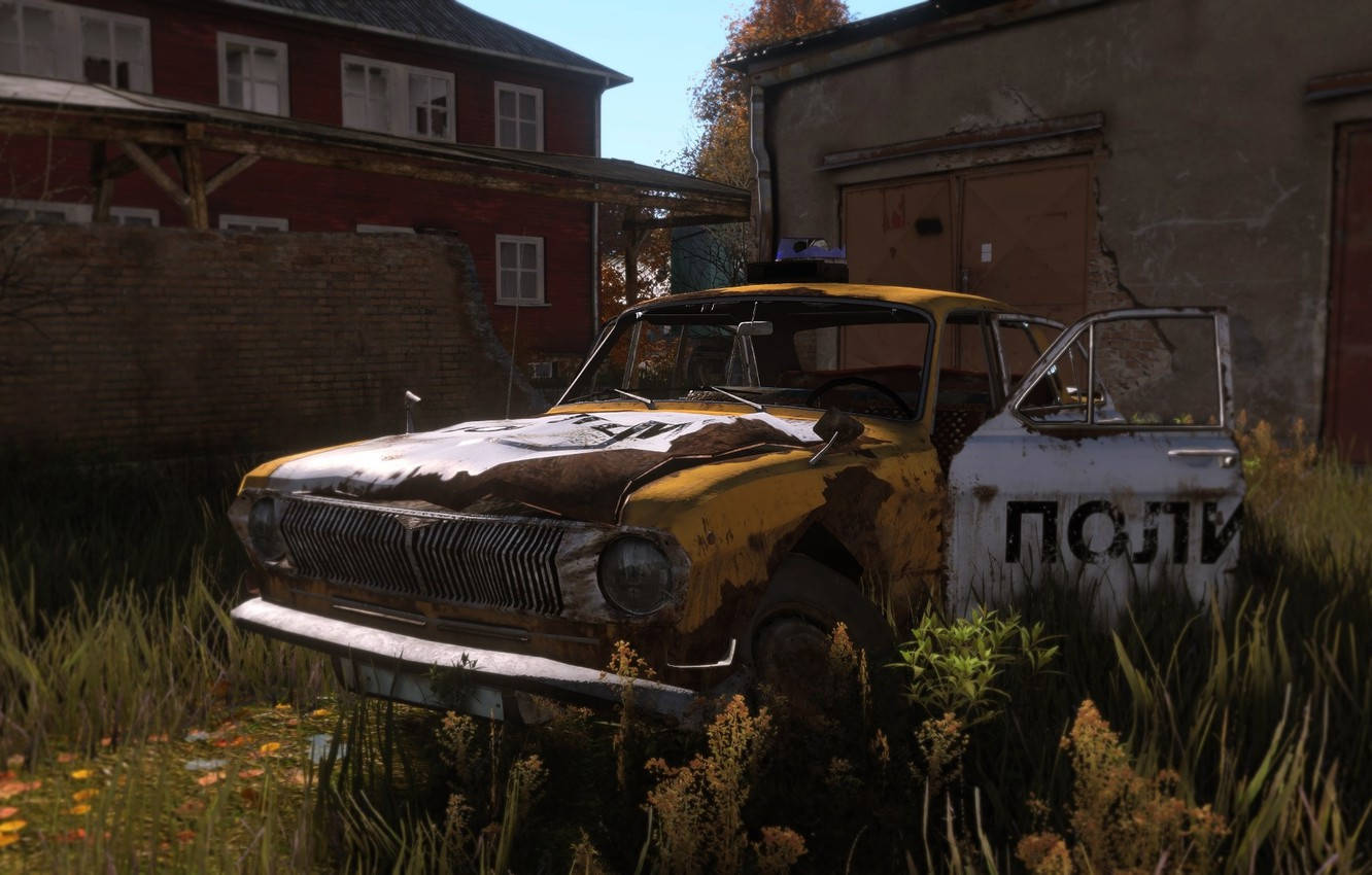 《DayZ》遺棄的計程車 壁紙 — 一輛生鏽的黃色警車被遺棄在雜草叢生的廢棄建築旁，在明亮的日光下。