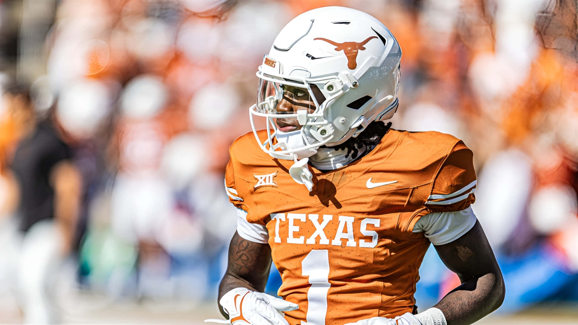  壁紙 — 一名德州長角牛美式足球員身穿橙色和白色裝備，在明亮的日光下專注地站在球場上。