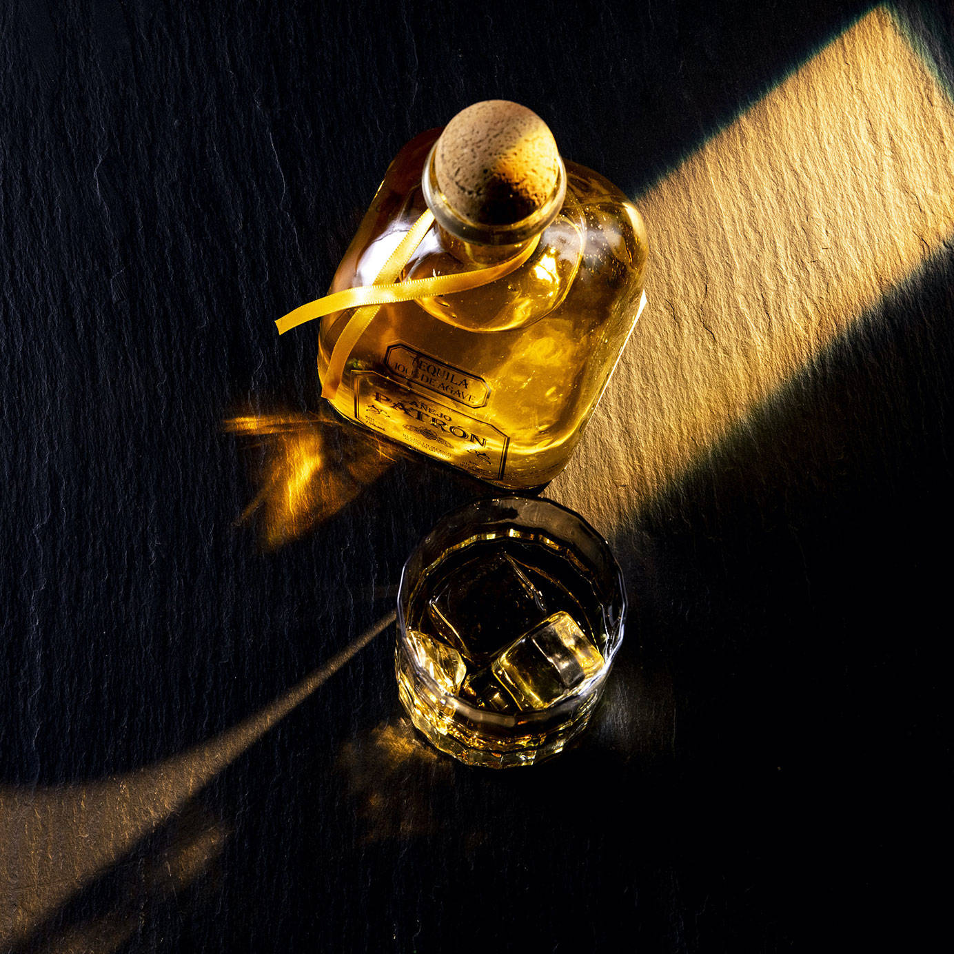 一瓶龍舌蘭酒和加冰的玻璃杯，在黑暗表面上被溫暖的陽光照射。