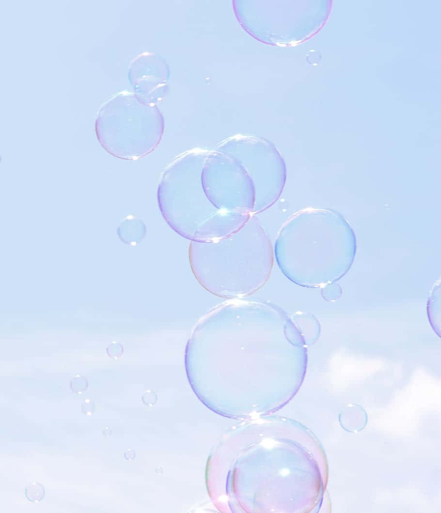  壁紙 — 精緻的彩虹色肥皂泡在柔和粉藍色天空和縷縷白雲中輕輕飄浮。