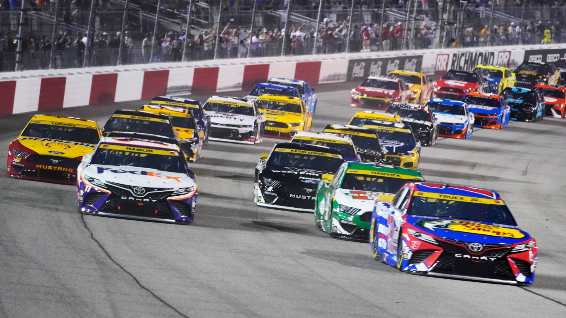 NASCAR賽車在夜間賽道上奔馳，伴隨著歡呼的粉絲。