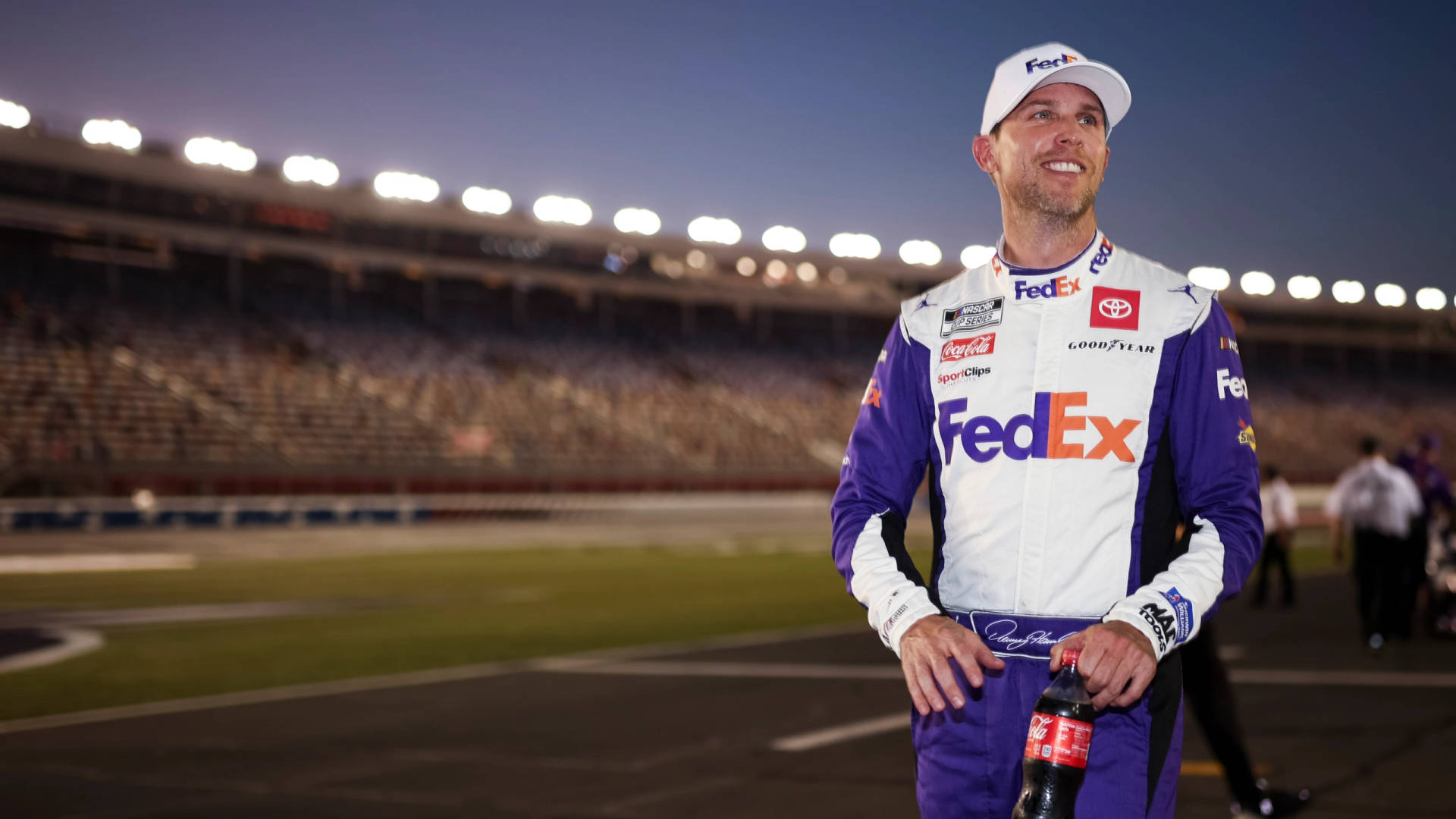 身穿FedEx制服的NASCAR車手在黃昏的賽道上手持可口可樂瓶。