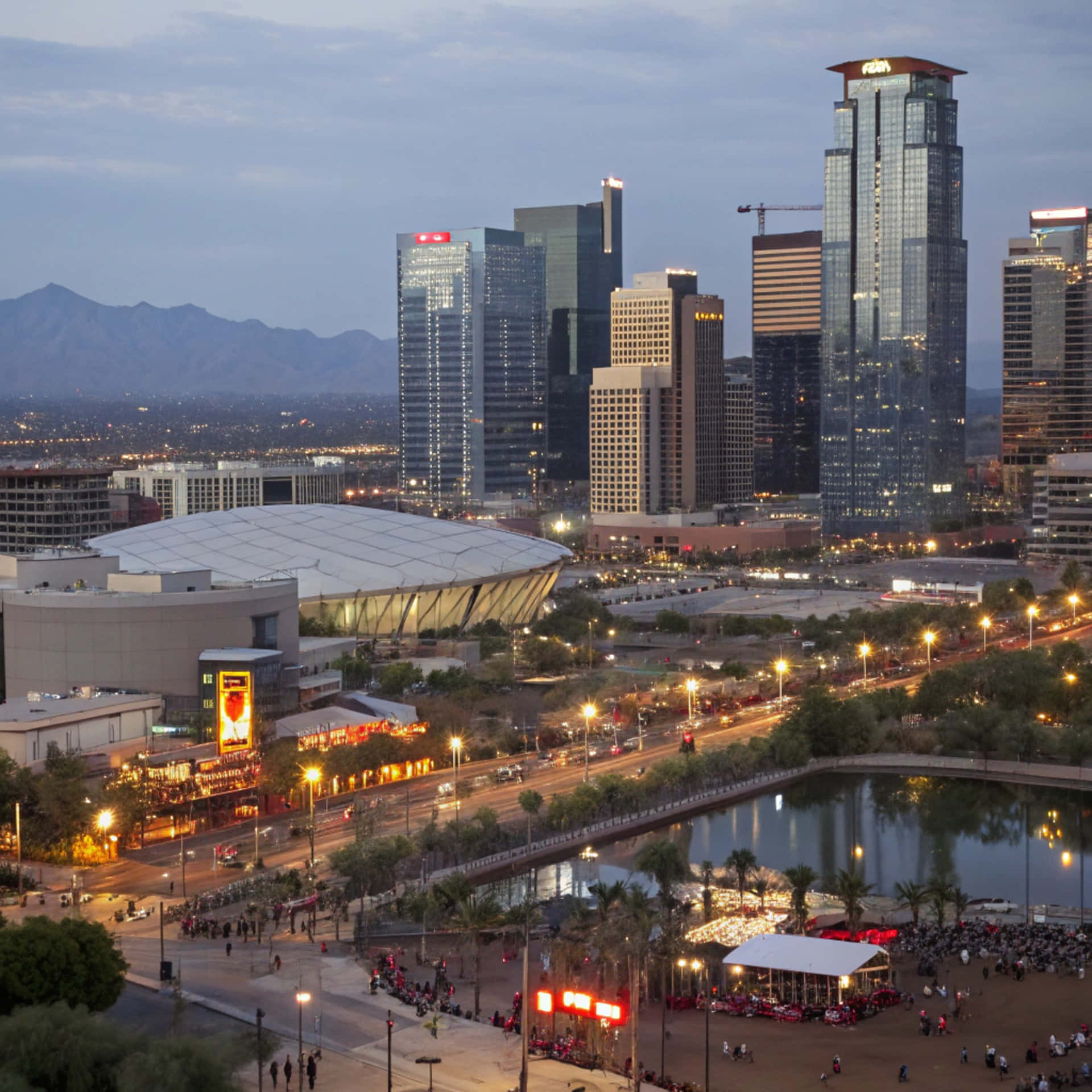 Denver Skyline 壁紙 — 黃昏城市景觀，包括燈火通明的摩天大樓、圓頂體育場以及充滿棕櫚樹和人潮的熱鬧海濱廣場。