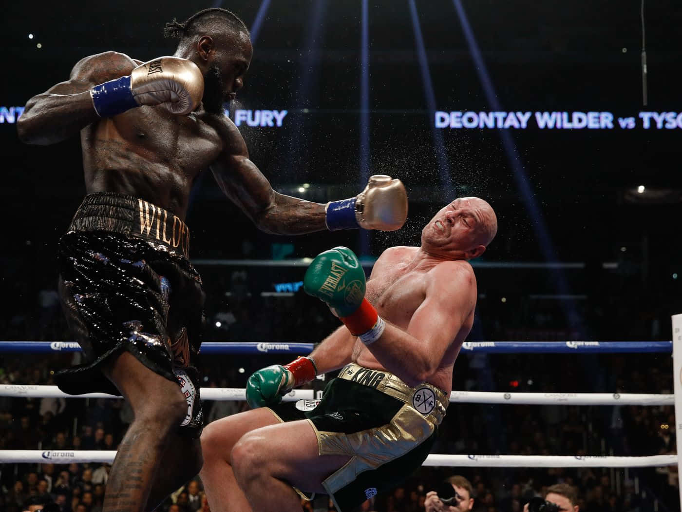  壁紙 — Deontay Wilder 在明亮的場館燈光下，於戲劇性的拳擊擂台上向 Tyson Fury 打出強力右勾拳。