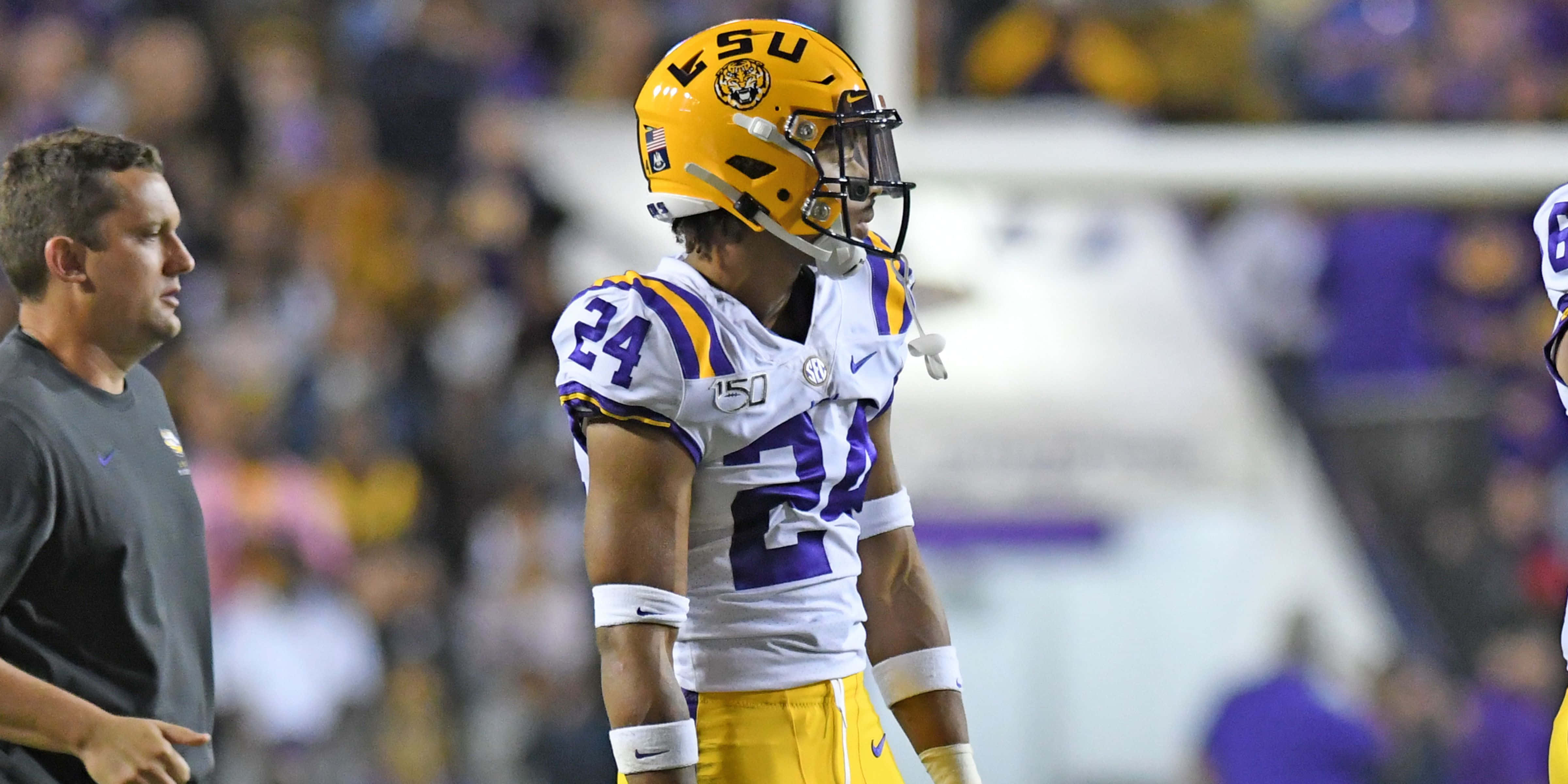 Derek Stingley Jr NFL 球隊選秀狀元 壁紙 — 一名身穿黃色和紫色裝備的LSU足球員在體育場燈光下比賽期間站在場上。