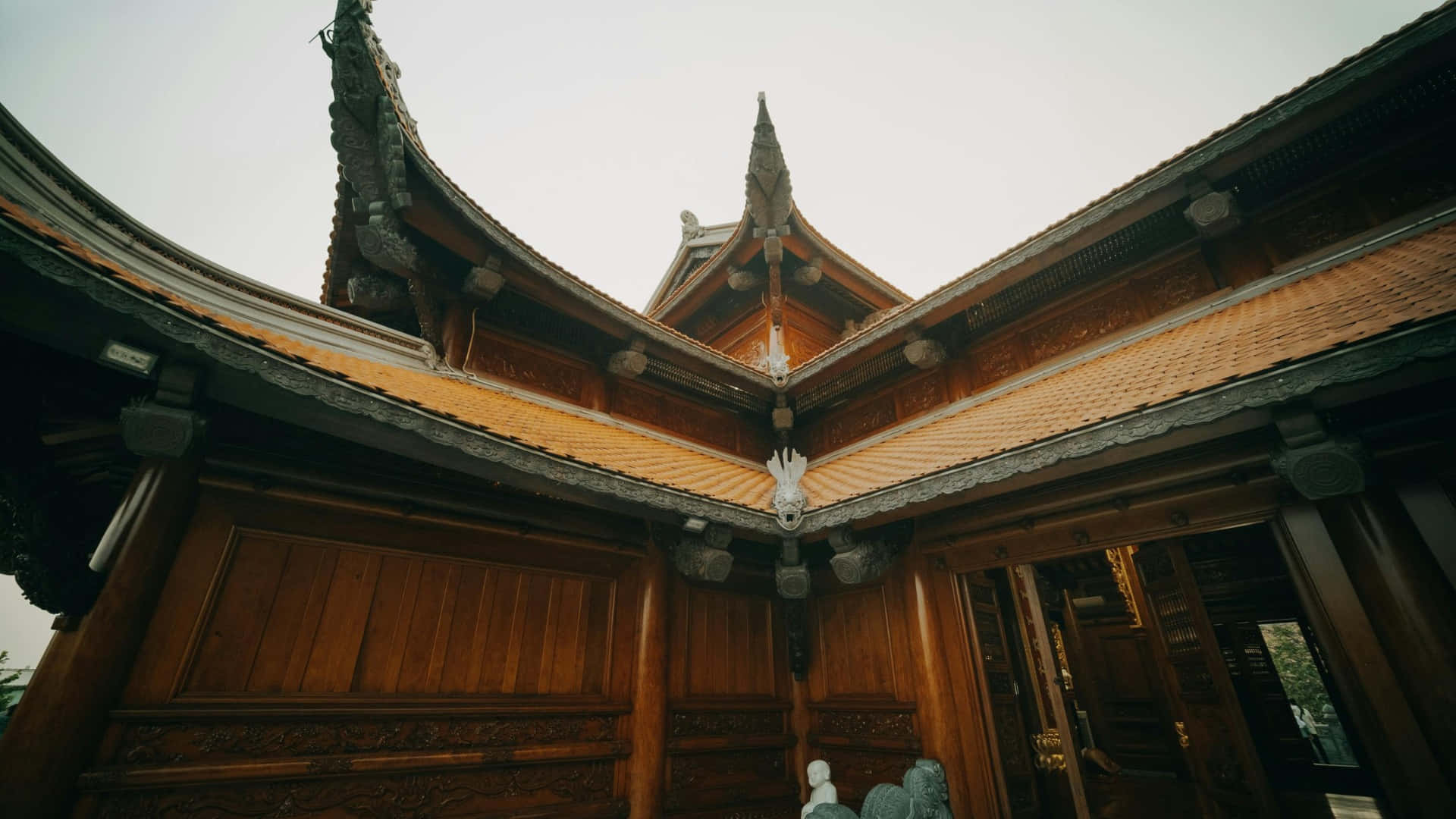  壁紙 — 低角度觀看多雲天空下裝飾華麗的木造寺廟屋頂，帶有彎曲的屋簷和複雜的雕刻。