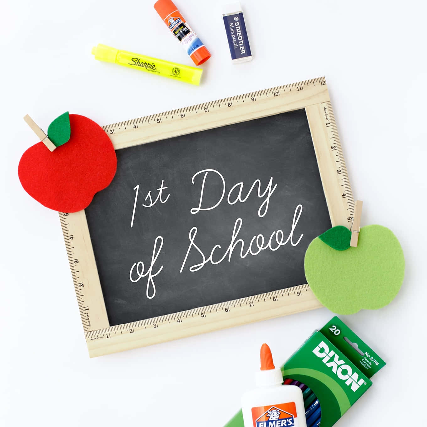  壁紙 — 一個木框黑板，上面用白色草書寫着「1st Day of School」，兩側有氈蘋果，周圍是白色背景上的學校用品。