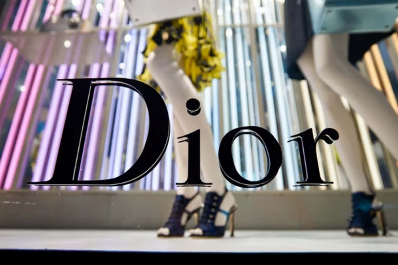 Dior時尚的優雅之美 壁紙 — Dior 標誌疊加在時尚的人體模型展示上，配有高跟鞋和色彩繽紛的垂直燈光，位於豪華商店櫥窗中。