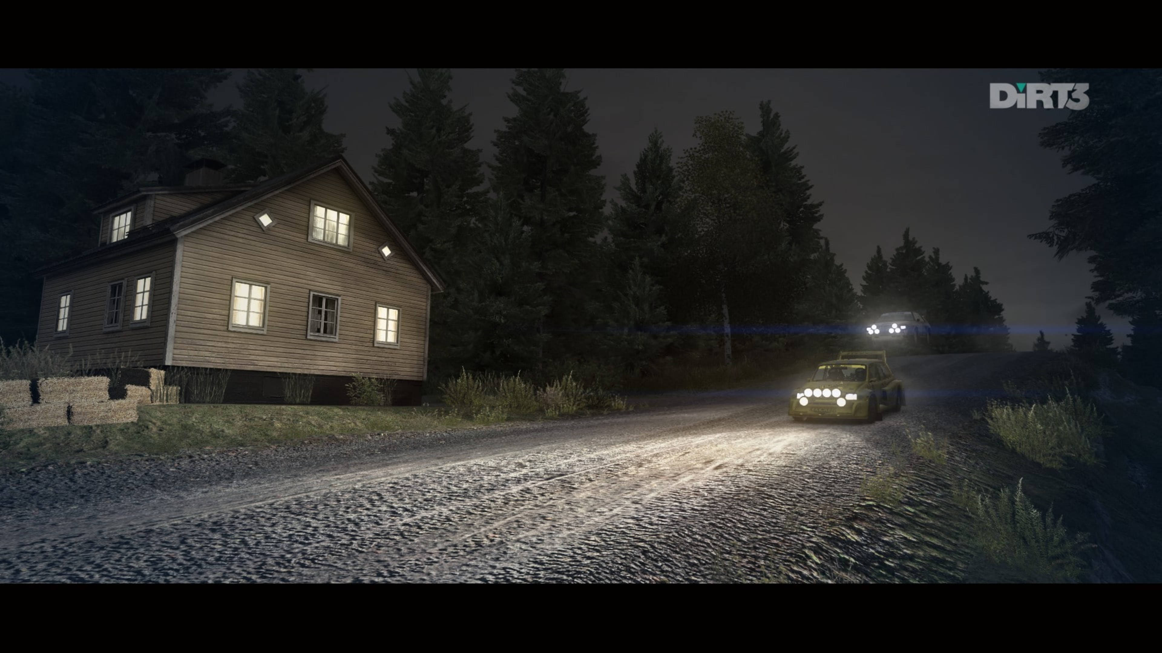 《Dirt 3》夜間賽車 壁紙 — 一輛帶有明亮頭燈的拉力賽車在夜間沿著碎石路行駛，經過一間被黑暗松樹環繞、燈光溫暖的木屋。