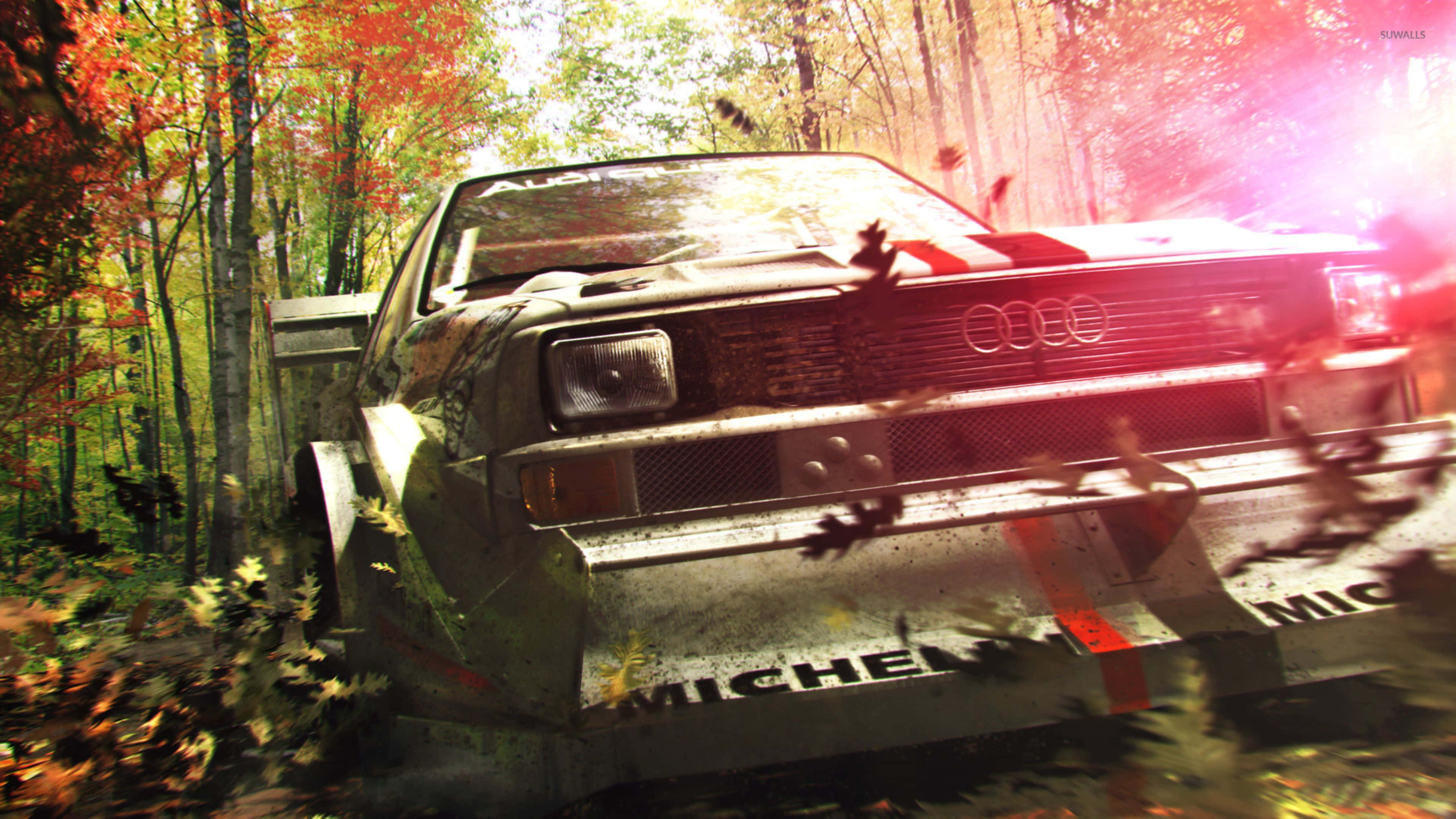 《DiRT 3》帶來心跳加速的拉力賽車體驗！ 壁紙 — 一輛泥濘的拉力賽車在充滿活力的秋日森林中疾馳，落葉飄飄，明亮的陽光穿過樹林。