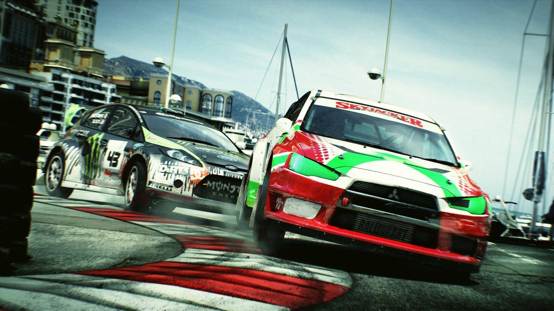 Dirt 3 面對決競賽高刺激 壁紙 — 兩輛拉力賽車在沿海賽道上激進飄移，背景有城市建築和山脈。