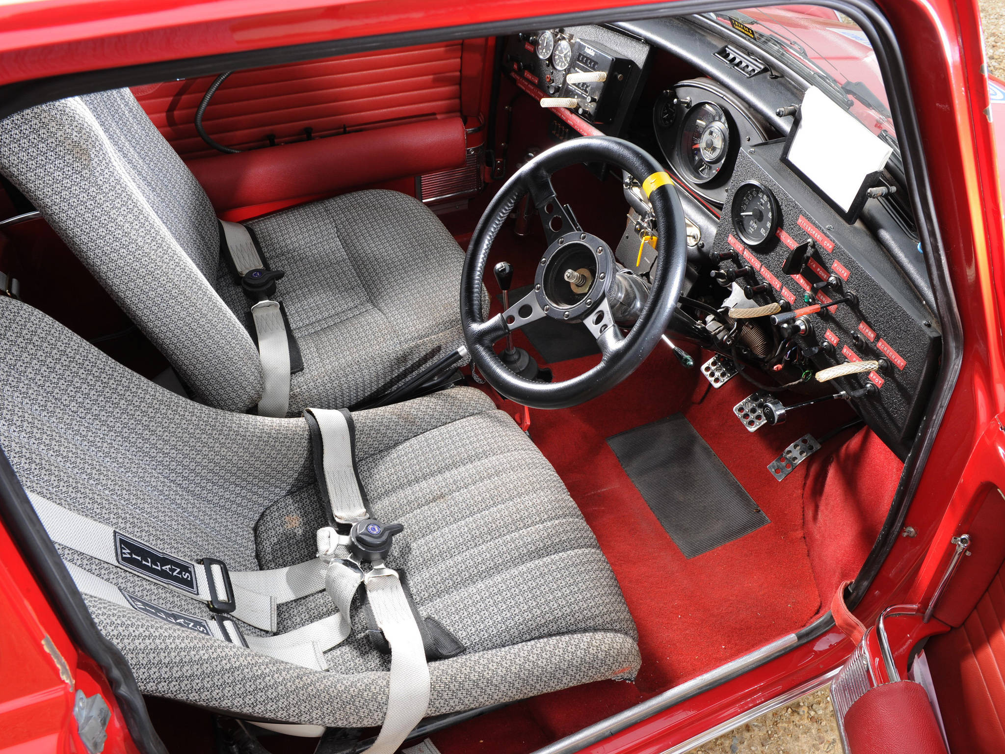 《Dirt Rally》賽車內部 壁紙 — 紅色復古賽車內飾，灰色圖案座椅和黑色方向盤。
