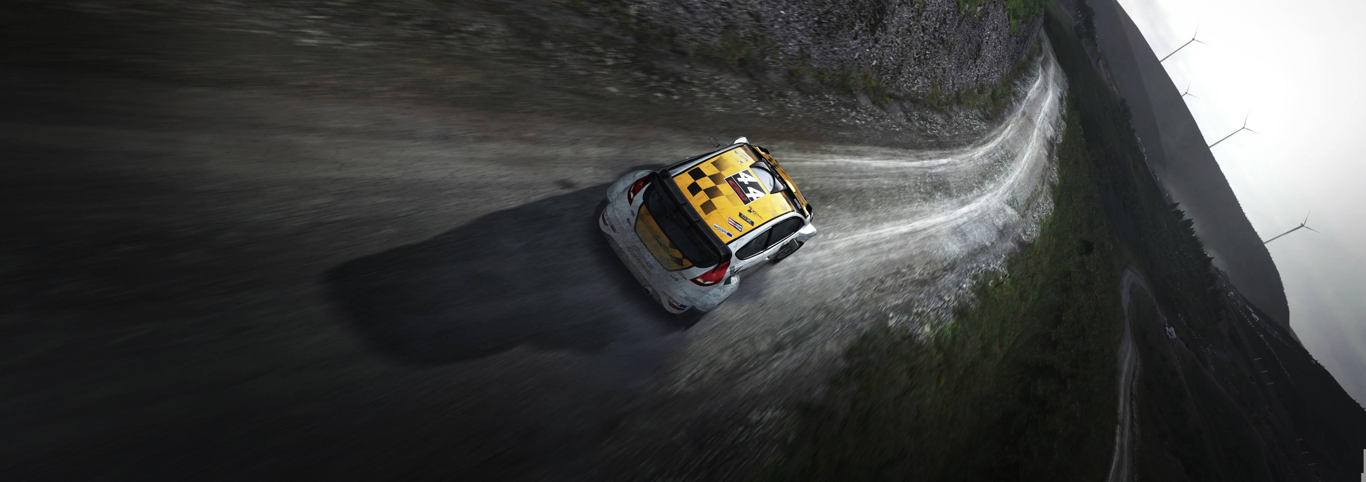 Dirt Rally 賽車行駛於泥濘路 壁紙 — 一輛黃黑相間的拉力賽車在霧氣繚繞的懸崖和遠處風力發電機的背景下，於陡峭的山路上飄移。