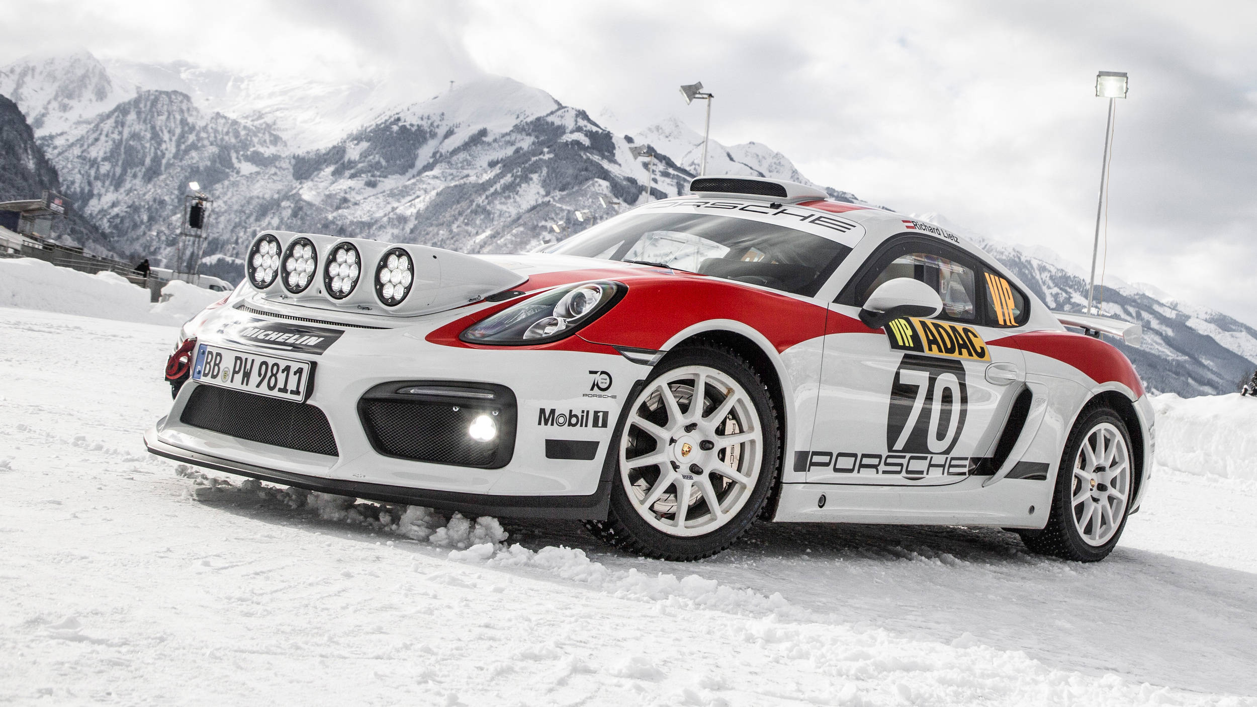 《Dirt Rally》遊戲中的Porsche 718 Cayman 壁紙 — 一架白色和紅色嘅保時捷Cayman賽車，車身編號70，停泊喺雪地之上，背景係白雪覆蓋嘅山脈。