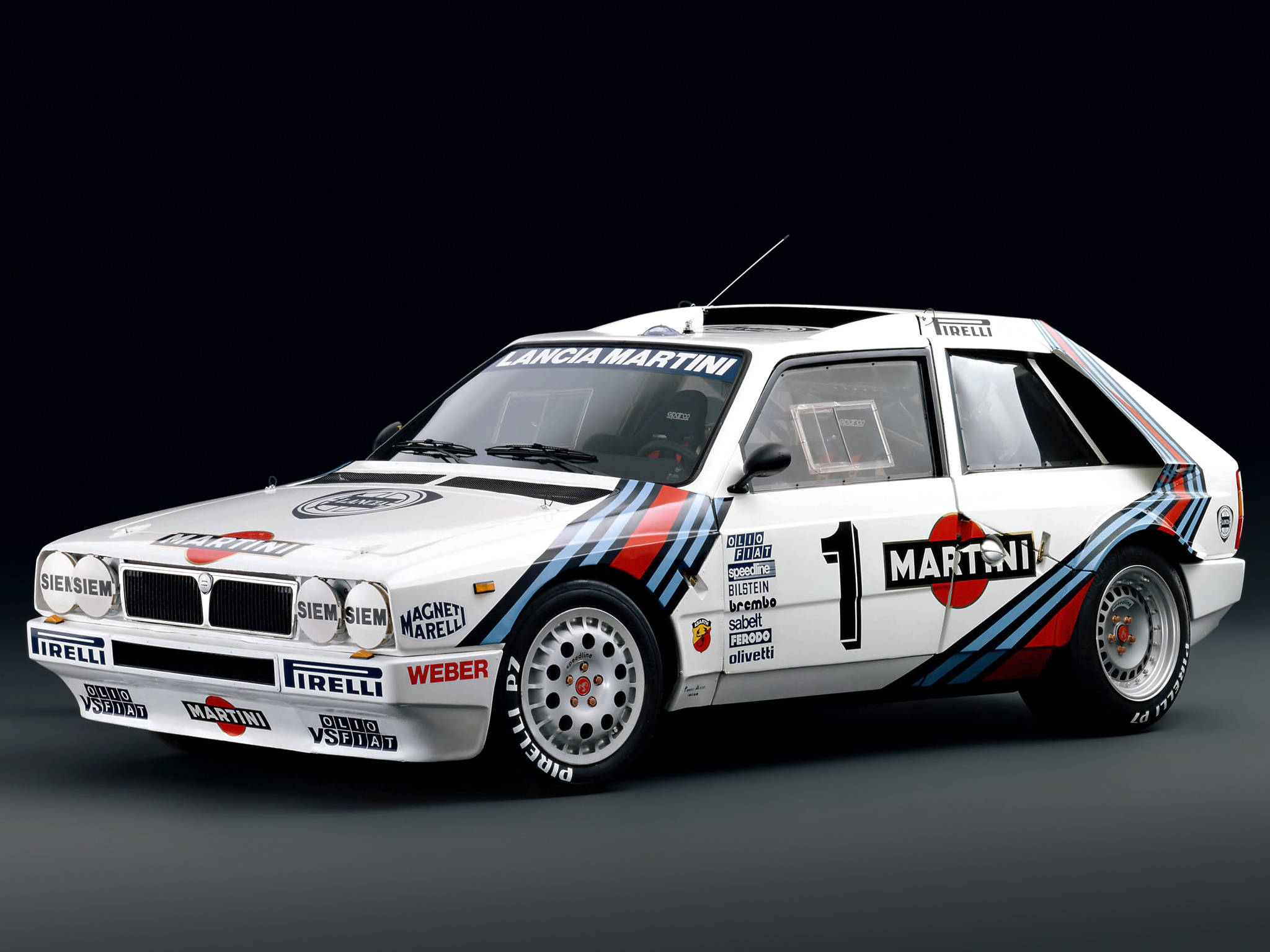 《Dirt Rally》Lantia Delta賽車 壁紙 — 一輛白色Lancia Delta S4拉力賽車，帶有Martini塗裝和1號車號，在深色工作室背景下蓄勢待發。