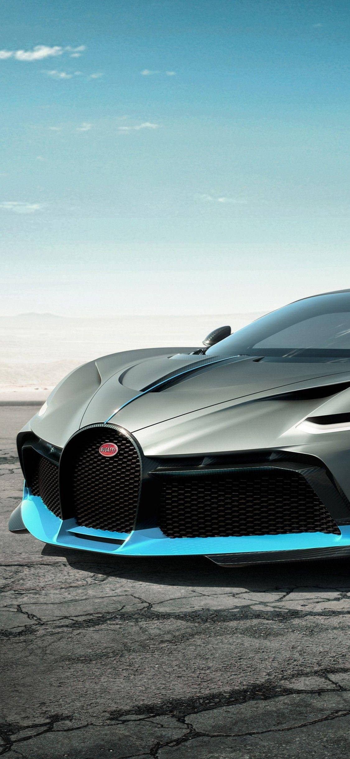 布加迪Divo iPhone汽車 壁紙 — 一輛時尚的銀色Bugatti超跑，帶有鮮豔的藍色點綴，停在晴朗藍天下破裂的瀝青路面上。