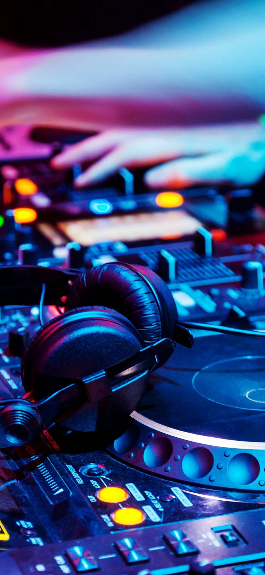 DJ Booth 音樂手機壁紙 壁紙 — DJ嘅手喺閃爍嘅唱盤同混音器上移動，被充滿活力嘅藍色同粉紅色霓虹燈淹沒。