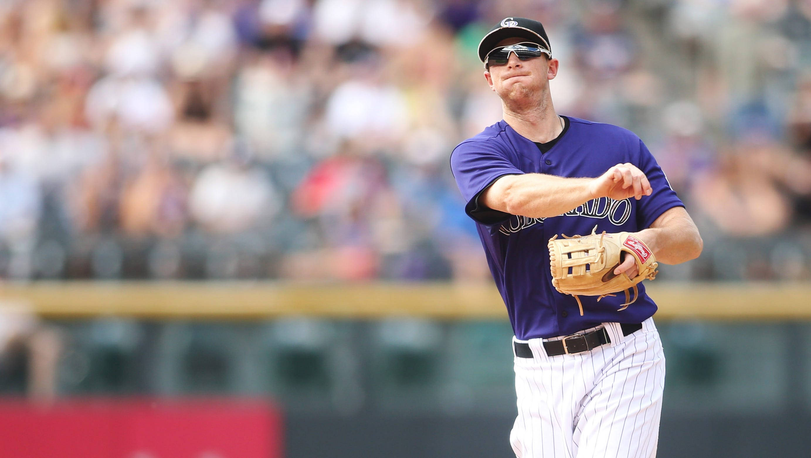 DJ LeMahieu 科羅拉多洛磯隊 壁紙 — 身穿紫色球衣的棒球投手在明亮的球場燈光下，背景是模糊的人群，準備投球。