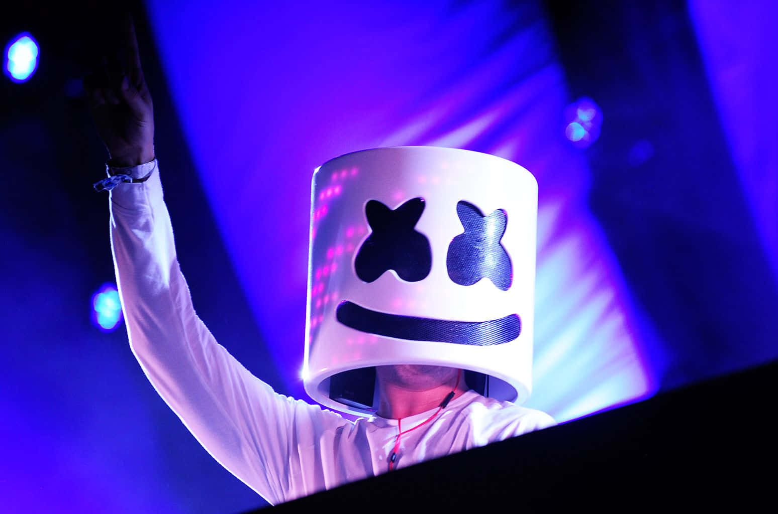 Marshmello 桌布 壁紙 — DJ Marshmello 在舞台上表演，戴著他標誌性的白色頭盔，在充滿活力的紫藍色燈光下，舉起一隻手臂。