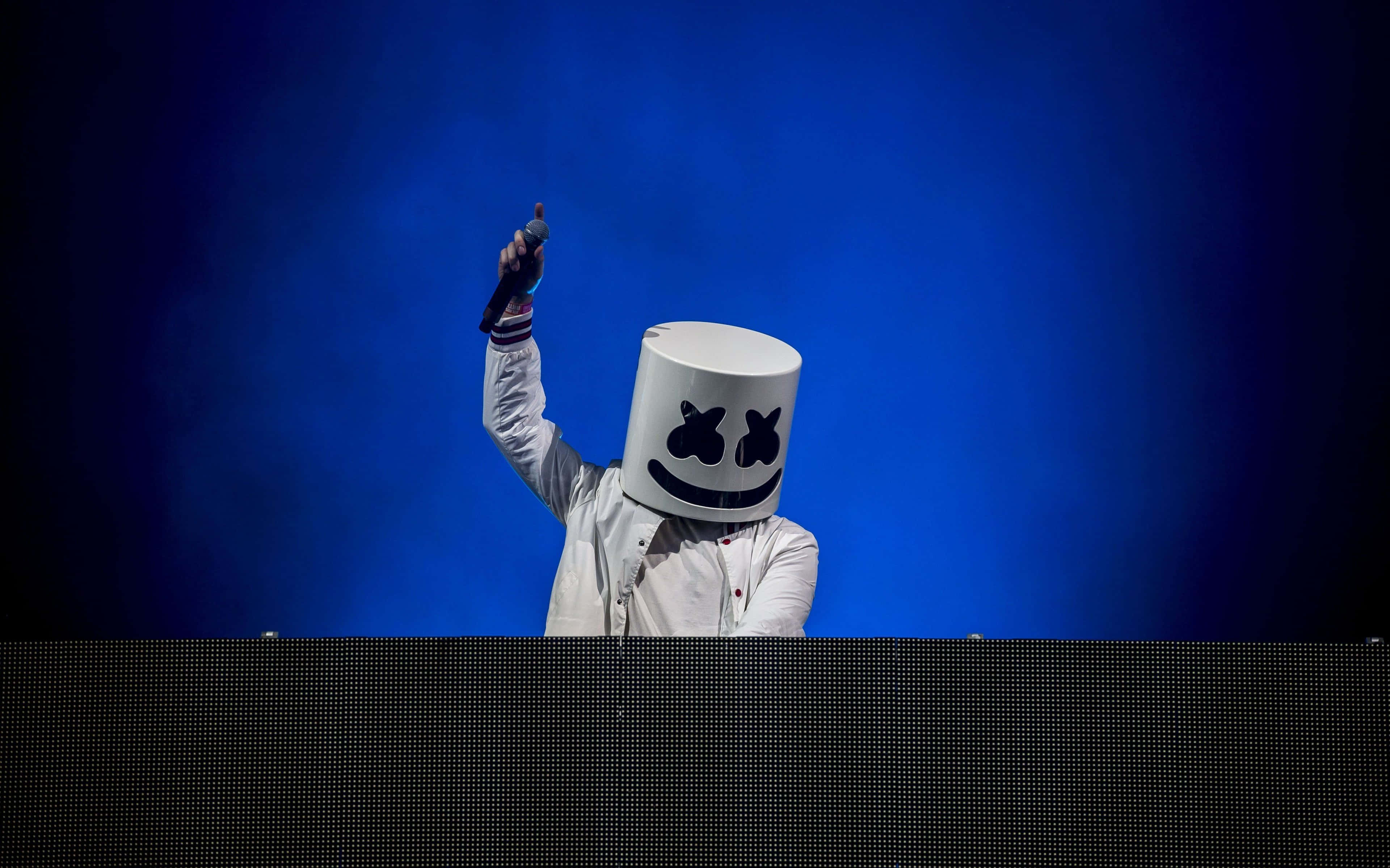 Marshmello 桌布 壁紙 — DJ Marshmello 戴著標誌性白色頭盔，在藍色燈光演唱會舞台上舉起手。