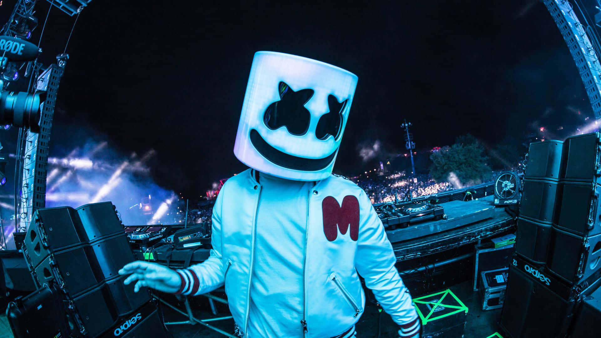 Marshmello 桌布 壁紙 — DJ Marshmello 穿著發光白色頭盔和外套，夜晚站在燈光璀璨的音樂會舞台上，背後有群眾和燈光。