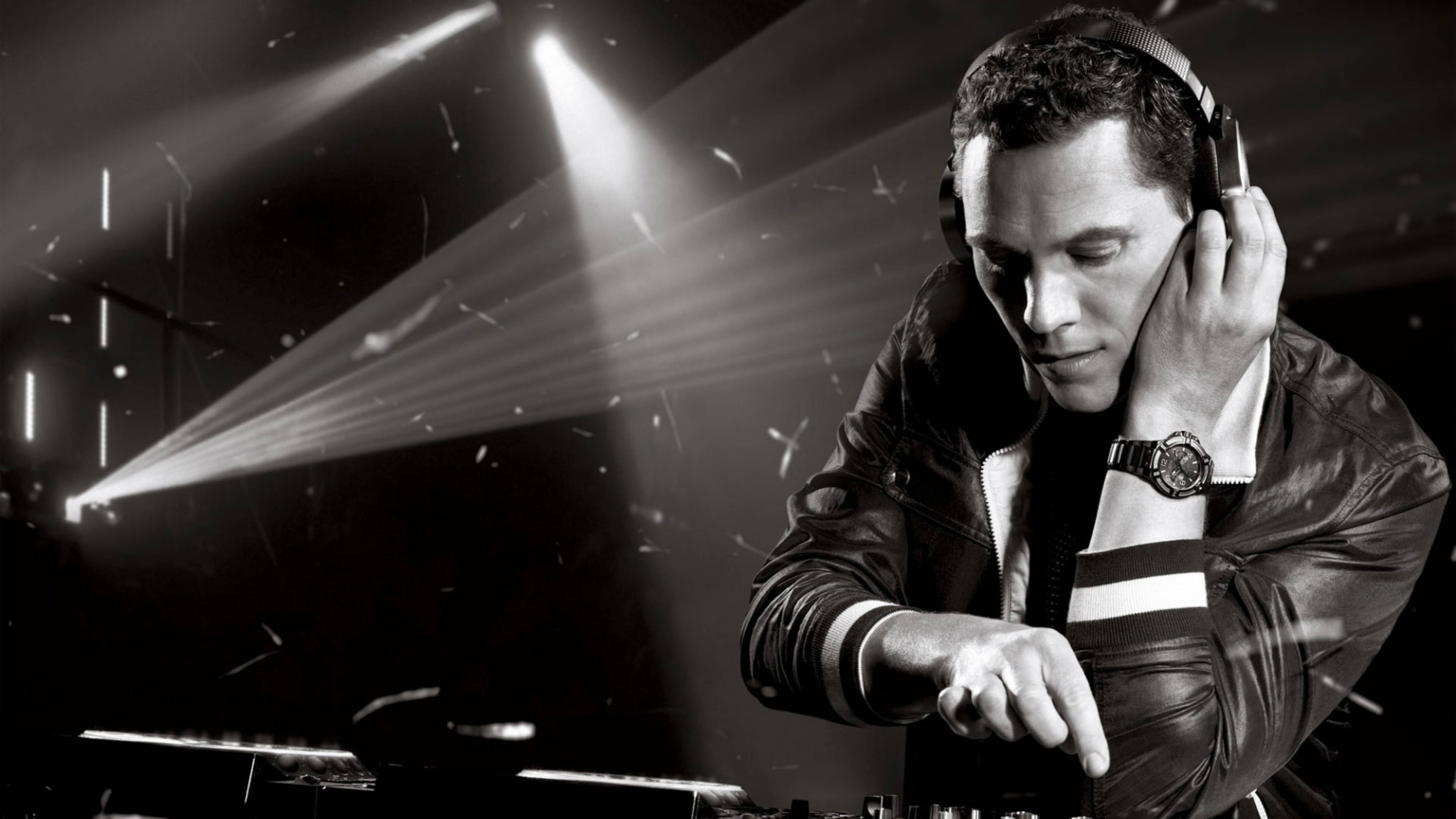 DJ Tiesto 黑色造型 壁紙 — 一位身穿皮褸的DJ在黑白戲劇性舞台聚光燈下專注於他的唱盤。