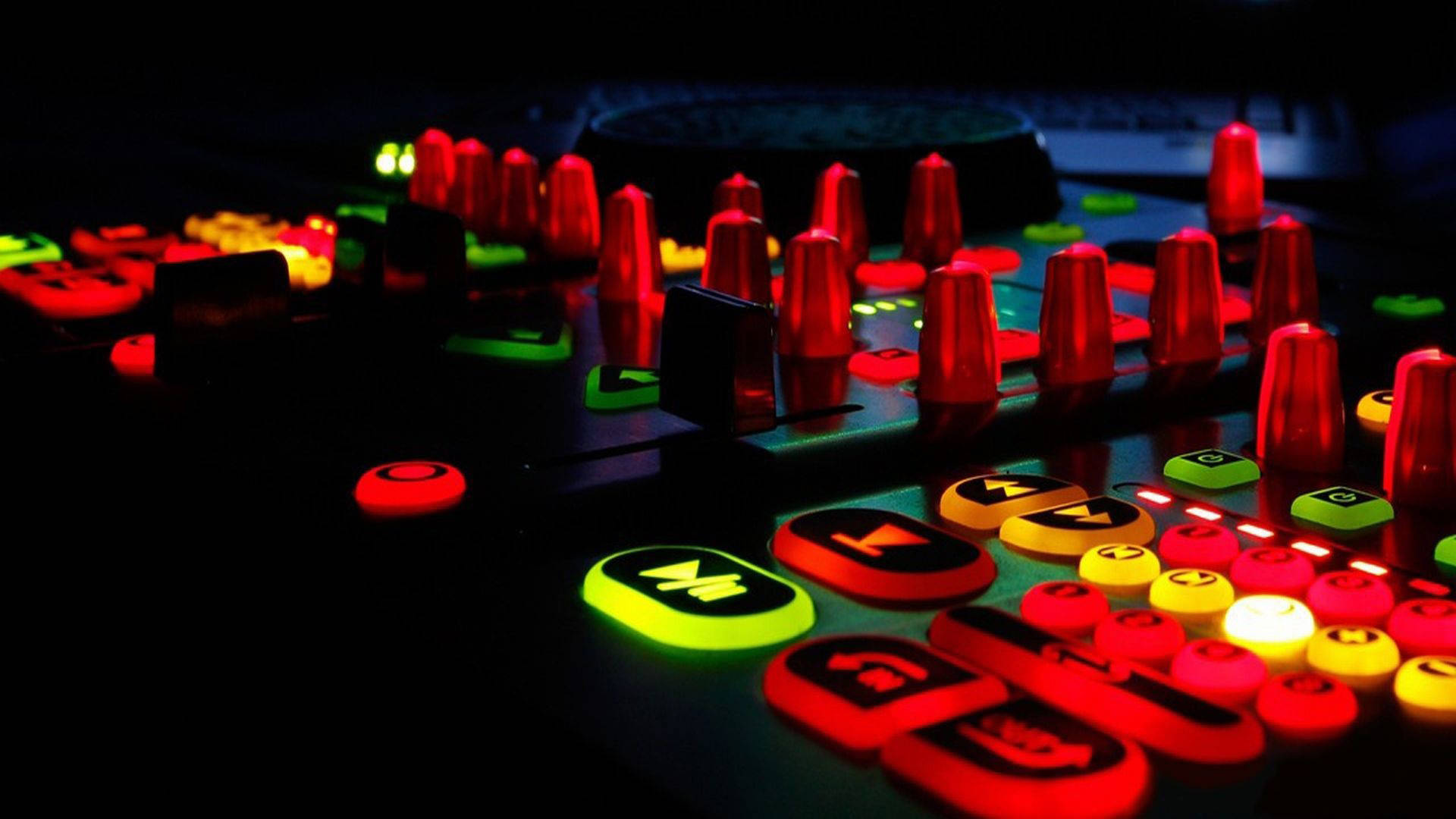 DJ 的酷炫音樂混音台 壁紙 — DJ混音器特寫，在昏暗的工作室中帶有發光的紅色、綠色和黃色按鈕及旋鈕。