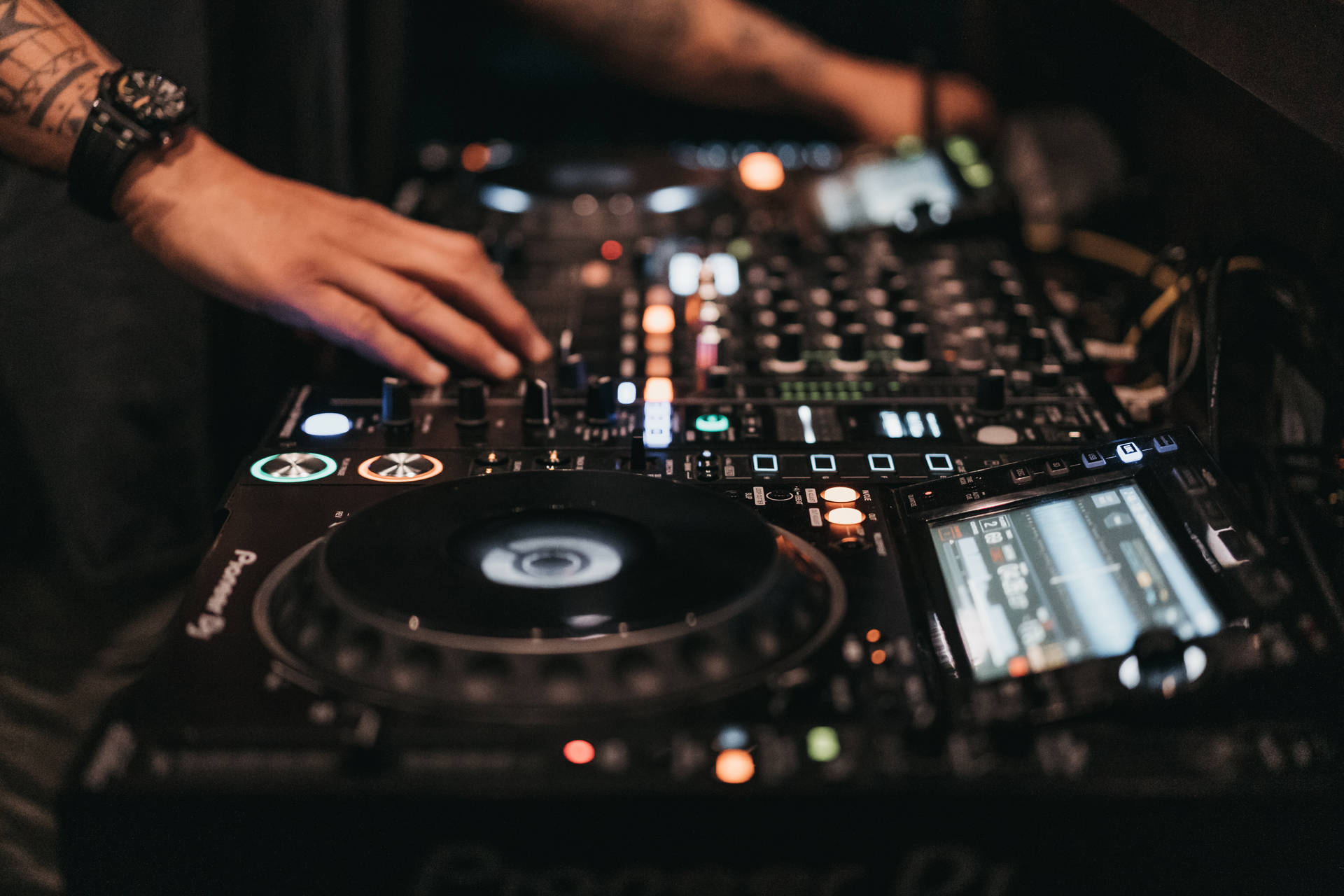 DJ手在黑暗的俱樂部環境中調整Pioneer DJ混音器上的控制。