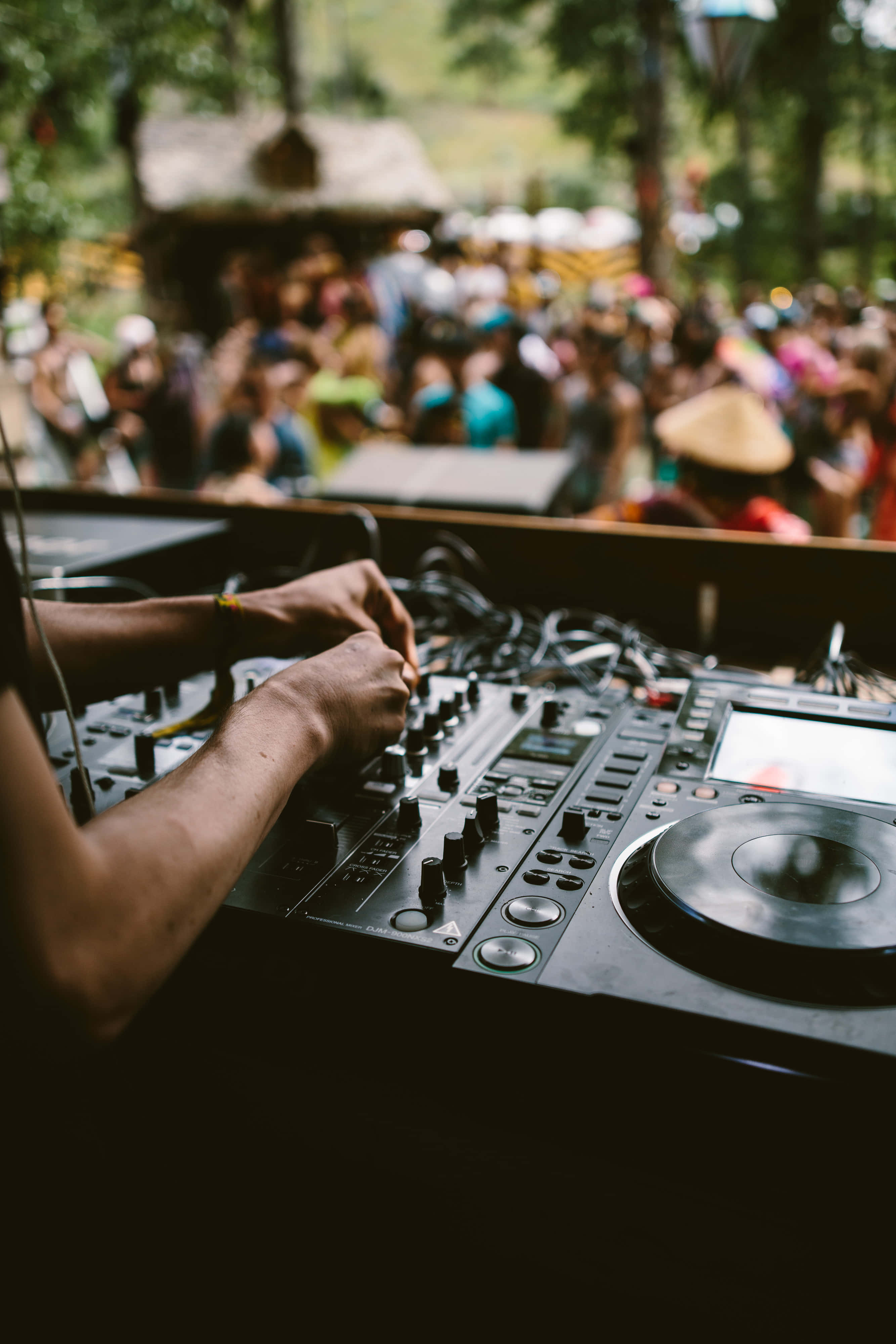 DJ 桌布 壁紙 — DJ嘅手熟練噉喺戶外音樂節上操控旋鈕同唱盤，背景係模糊嘅人群。