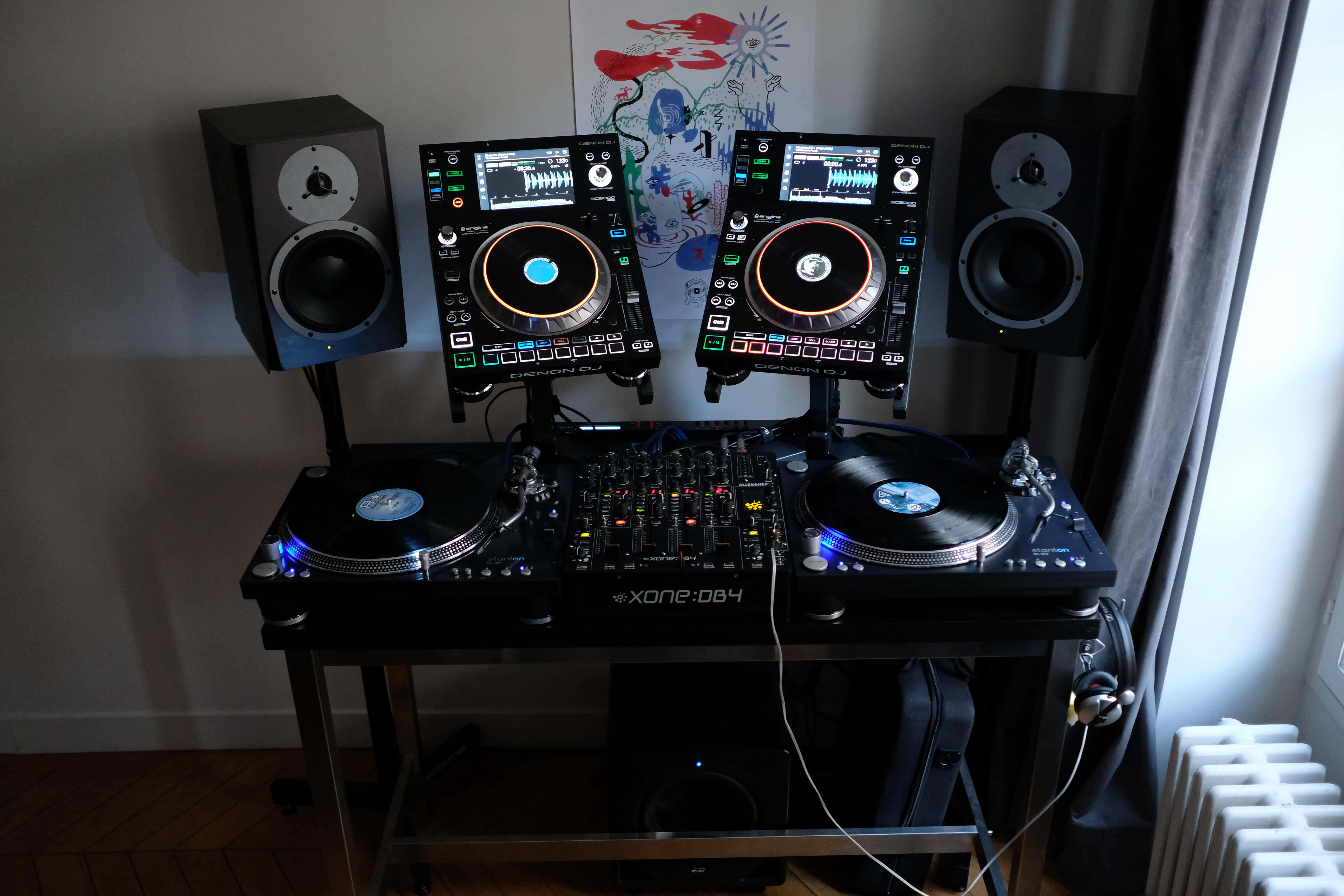 DJ工作室居家揚聲器音樂設置圖片 壁紙 — 專業DJ設置，配備兩個唱盤和控制器，在昏暗房間的環境光下發光。