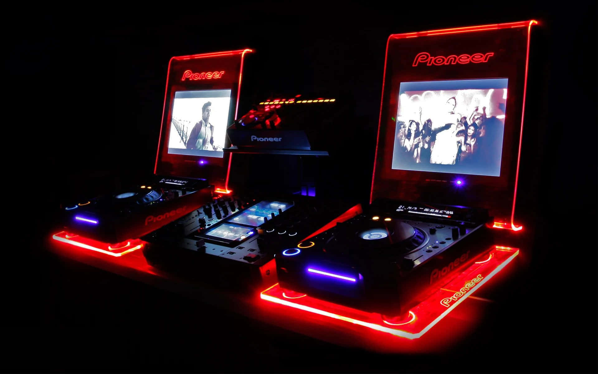 DJ舞臺視頻轉盤設置圖 壁紙 — 兩個 Pioneer DJ 唱盤在黑色背景上發出紅藍光芒，屏幕上顯示人群和表演者的視覺效果。