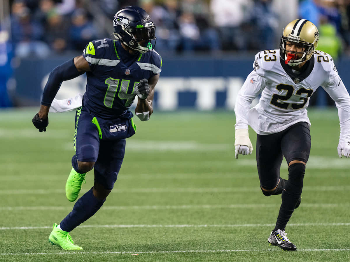 DK梅特卡夫與馬許恩·拉蒂莫爾 壁紙 — 兩名NFL球員在充滿活力的綠色場地上衝刺，一人身穿深藍色配螢光綠色點綴，另一人身穿白色和金色，展開激烈競爭。