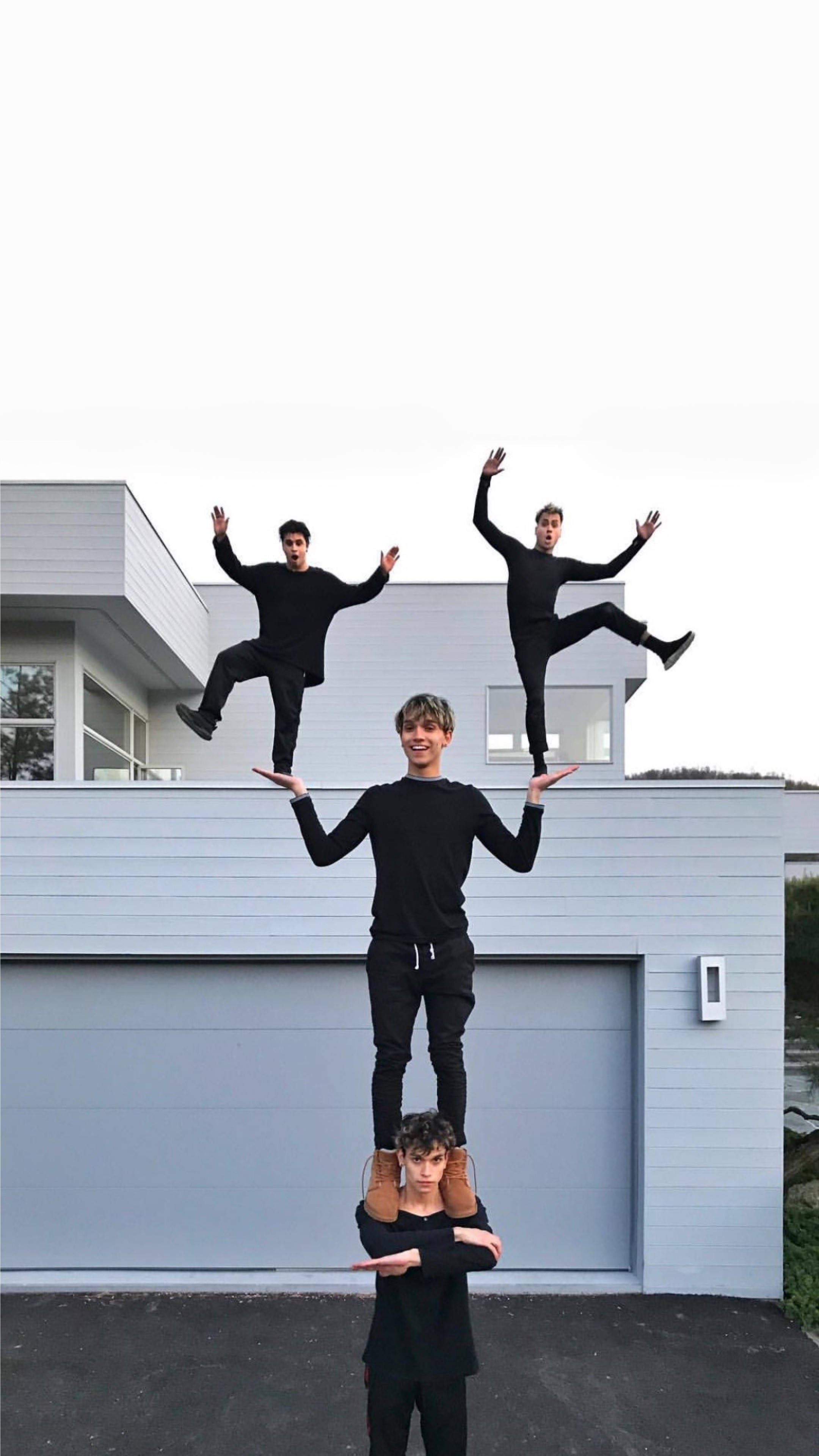 Dobre Brothers 的耍酷姿勢 壁紙 — 四名身穿黑色服裝的年輕男子在現代灰色房屋外伸出雙臂形成人體金字塔。
