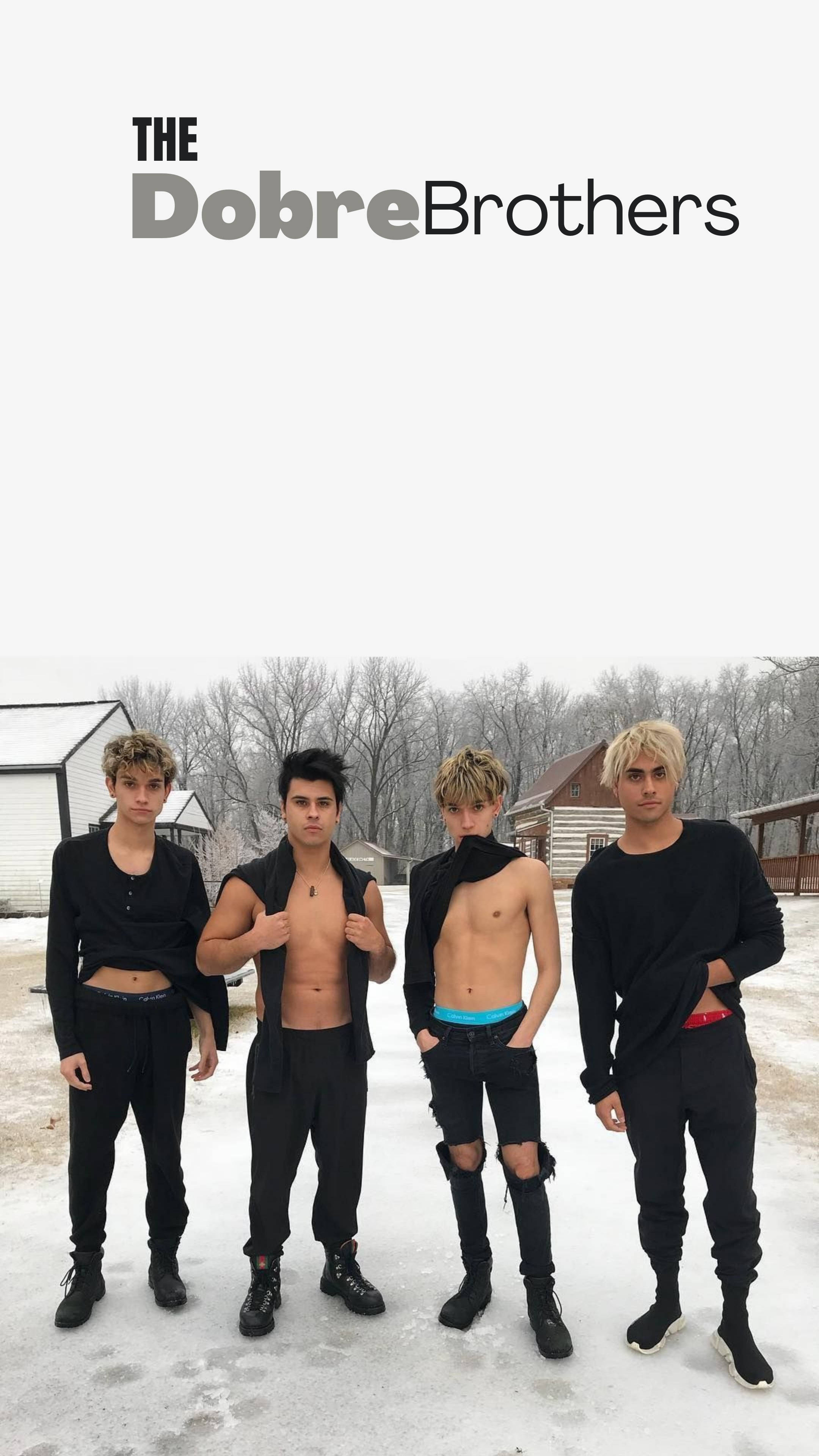 Dobre兄弟雪中冒險 壁紙 — 四個身穿黑色服裝的年輕男子自信地站在雪地上，背後是光禿禿的樹木和質樸的建築。