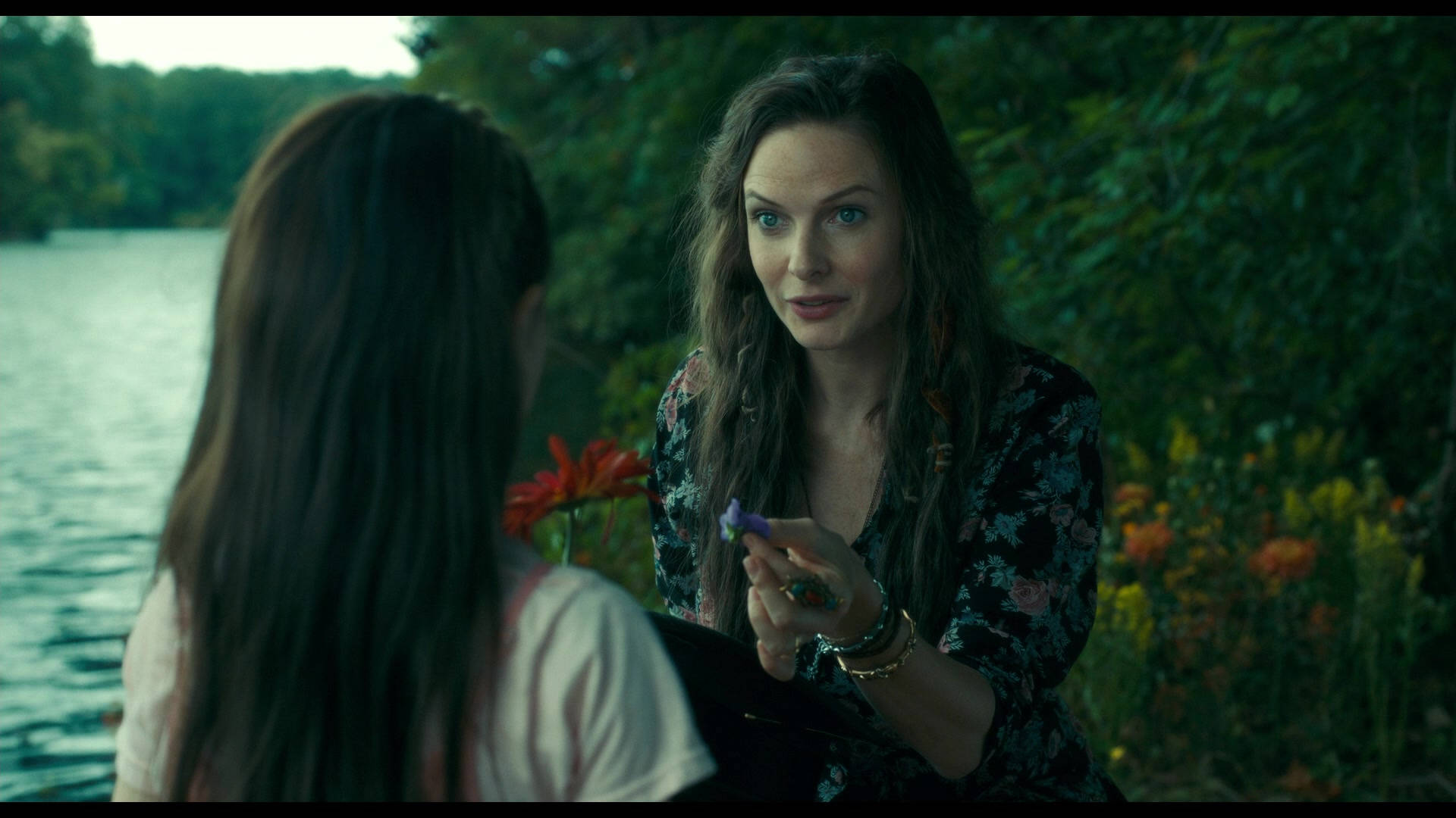 Doctor Sleep 美麗的 Rose 壁紙 — 一位長黑髮的女性坐在湖邊，手持紫色花朵，正在與另一個人交談。