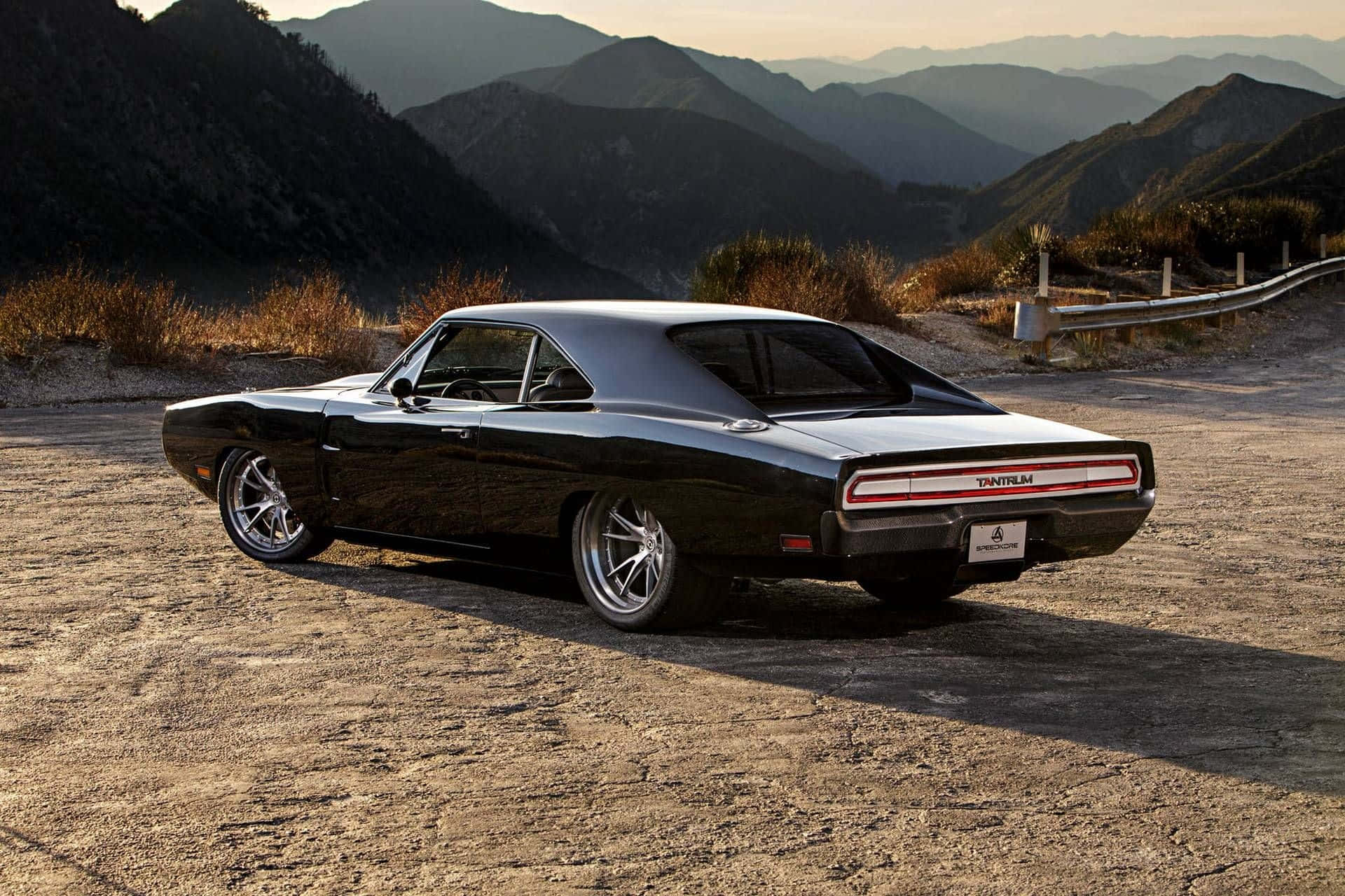  壁紙 — 一架型格黑色Dodge Charger Daytona停泊在塵土飛揚的山路上，背景有崎嶇山峰和金色光線。