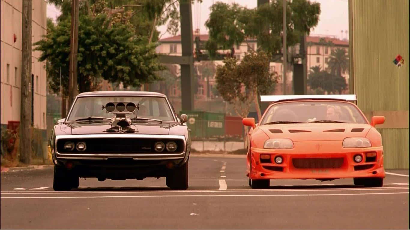 Dodge 與 Supra 最佳《速度與激情》背景 壁紙 — 兩輛標誌性的肌肉車在陽光明媚、兩旁種滿樹木和建築物的城市街道上對峙。