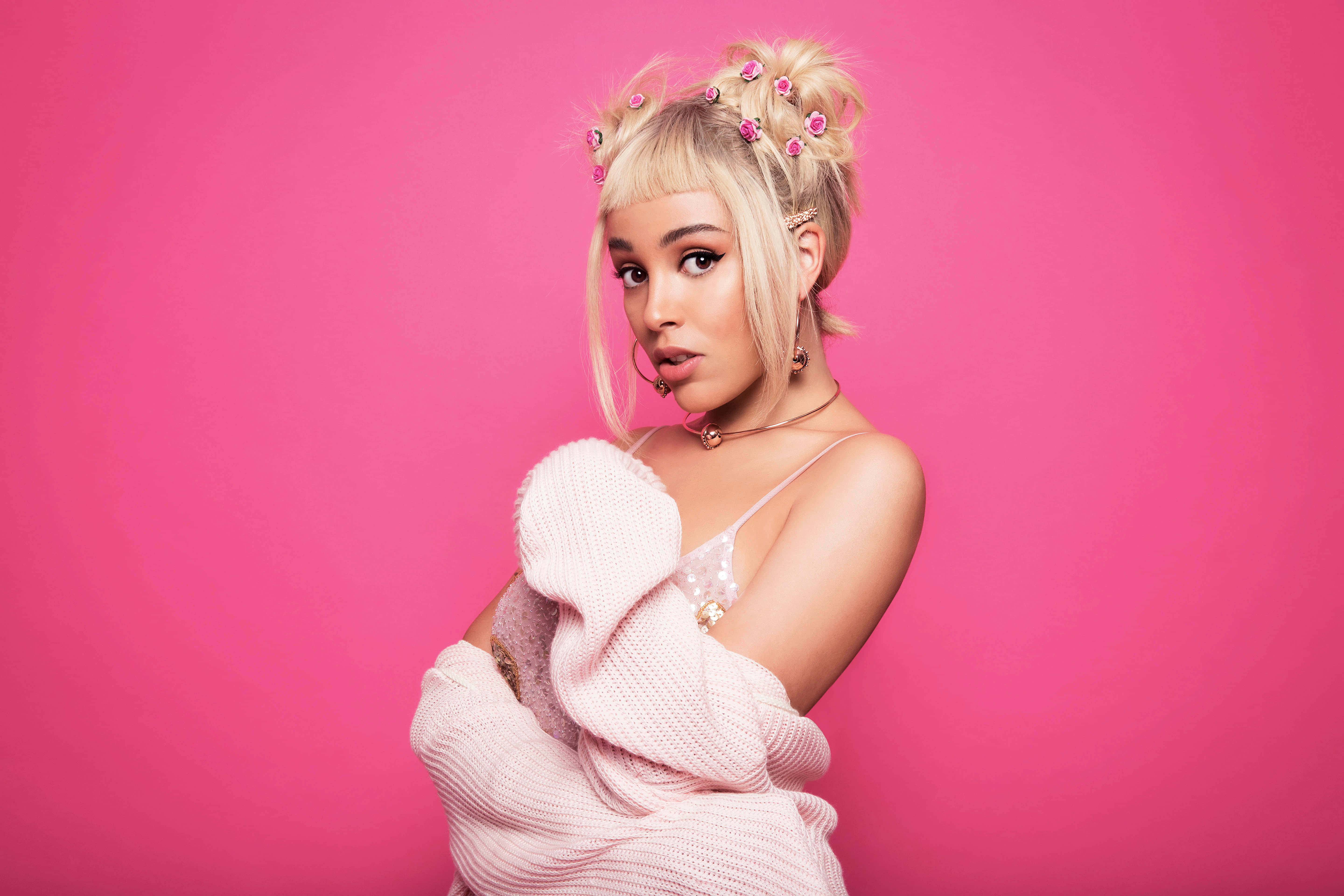 Doja Cat 追求星光 壁紙 — 一位金髮女子戴著粉紅色花卉髮飾，穿著舒適的粉紅色毛衣，在充滿活力的粉紅色攝影棚背景前自信地擺姿勢。