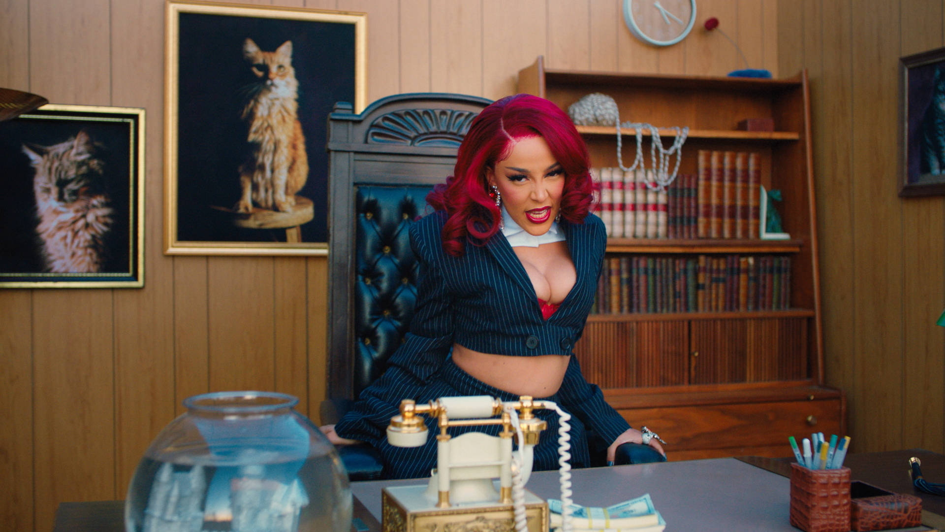 Doja Cat 女強人辦公室 壁紙 — 一位擁有鮮豔紅髮的女性自信地坐在復古辦公椅上，身後桌上放著復古電話和魚缸。