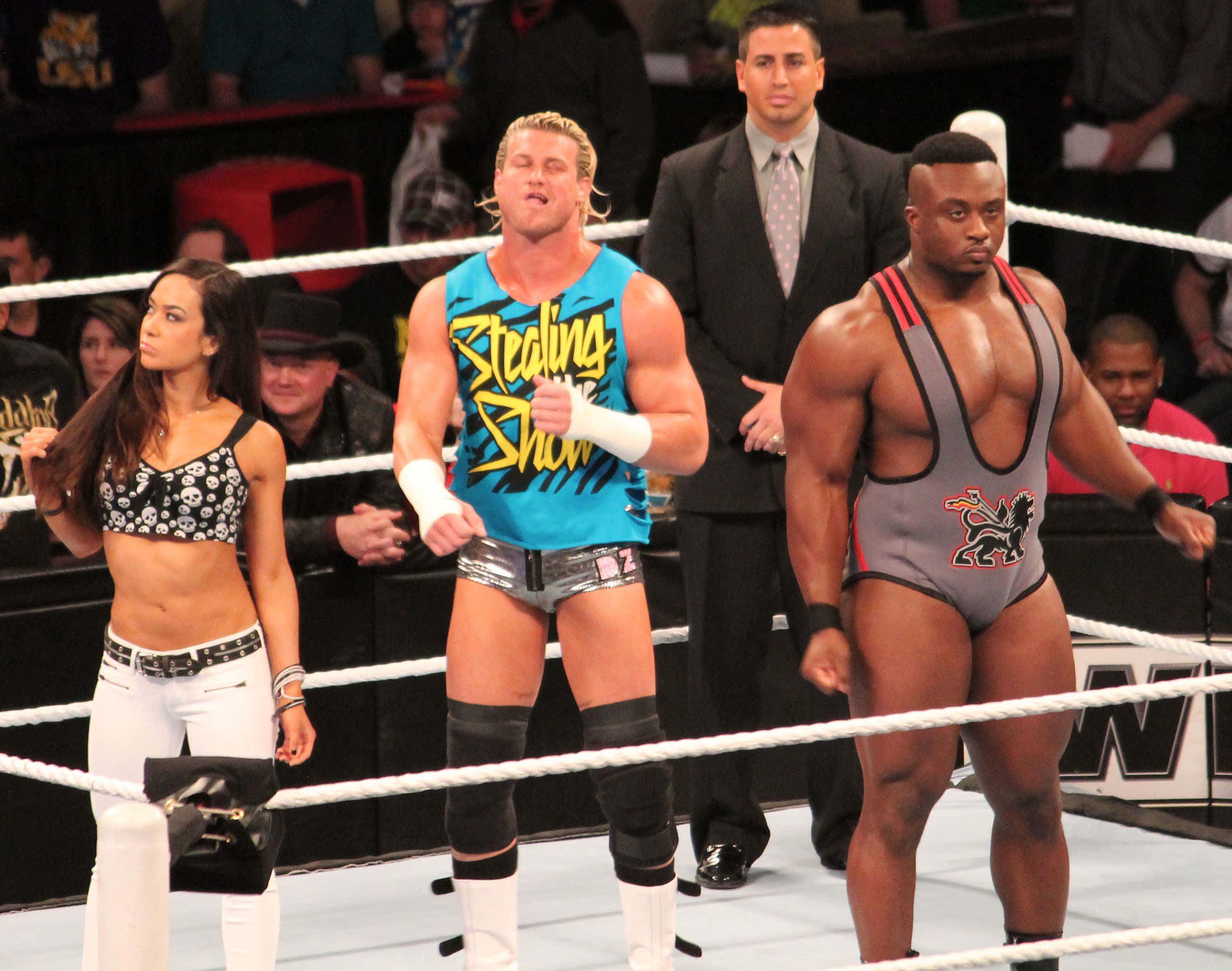 Dolph Ziggler、AJ Lee與Big E Langston 壁紙 — 三名摔角手和一名女子站在有繩索的擂台上，下方是明亮的場館燈光。
