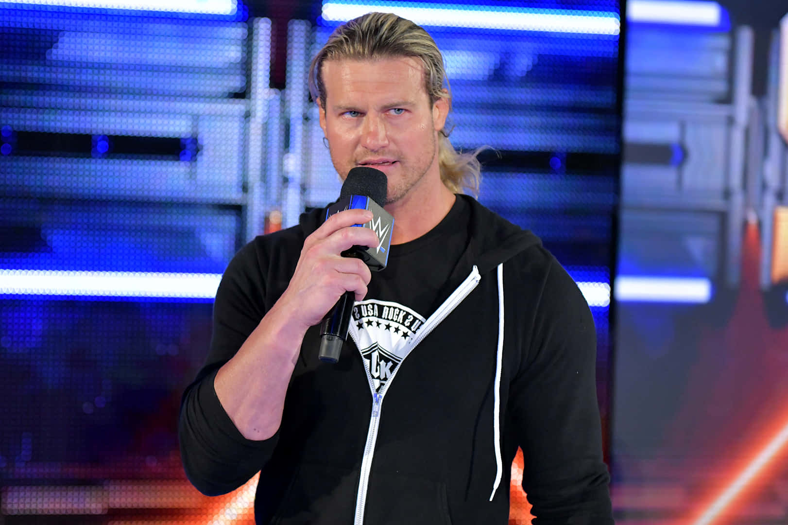 Dolph Ziggler Two-time Intercontinental Champion 壁紙 — 一位金髮摔角手在藍色燈光舞台背景前手持麥克風。