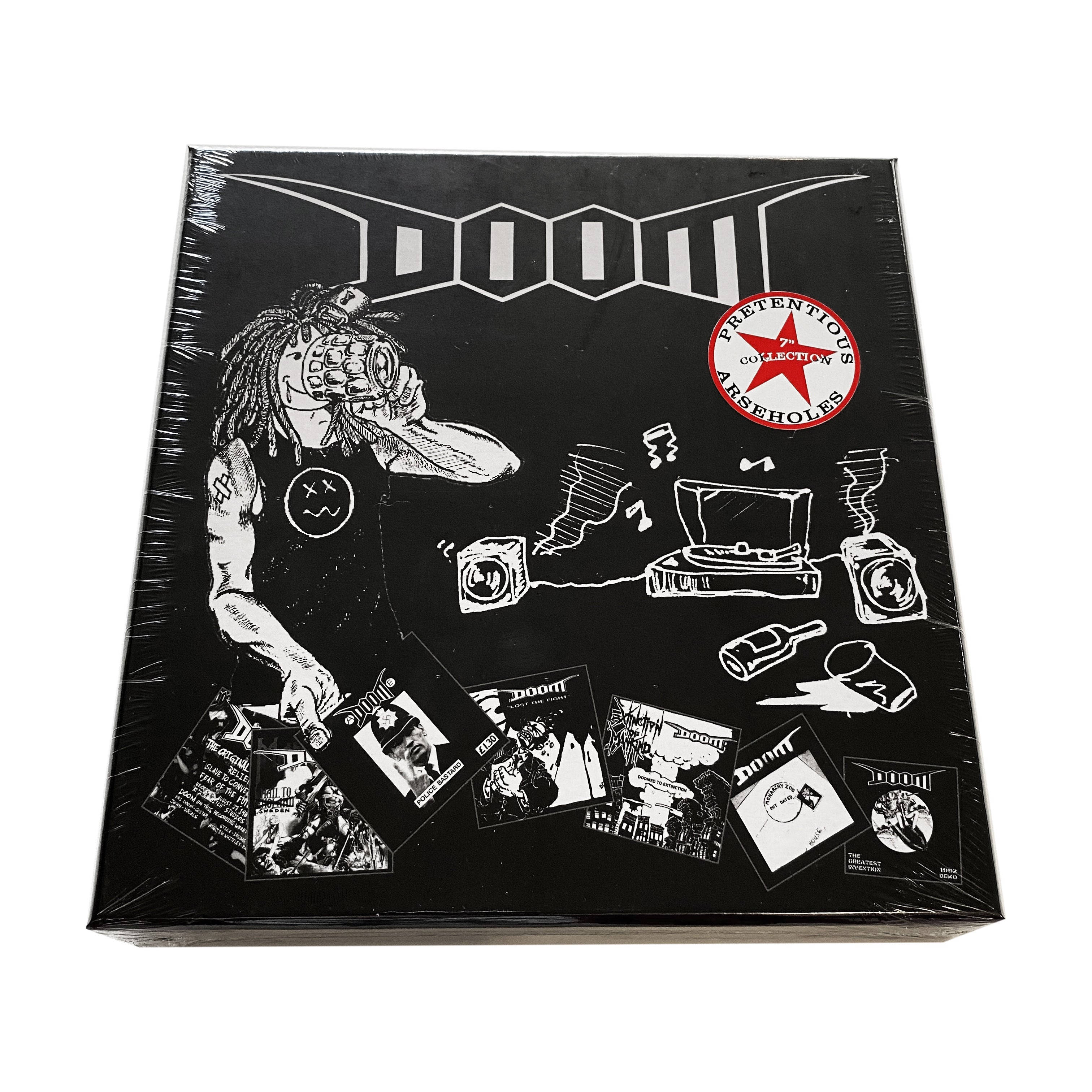 Doom《誇張混蛋》專輯封面俯拍 壁紙 — 一個黑白插圖的DOOM盒子，有一個塗鴉風格的角色拿著相機，周圍散落著專輯封面和一個紅色星星貼紙。