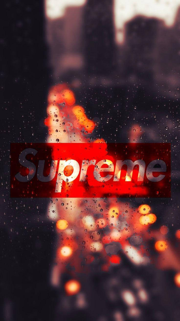 Dope Supreme 城市夜景 壁紙 — 一個紅色Supreme標誌透過沾滿雨水的窗戶發光，窗外是夜晚模糊的城市景觀。