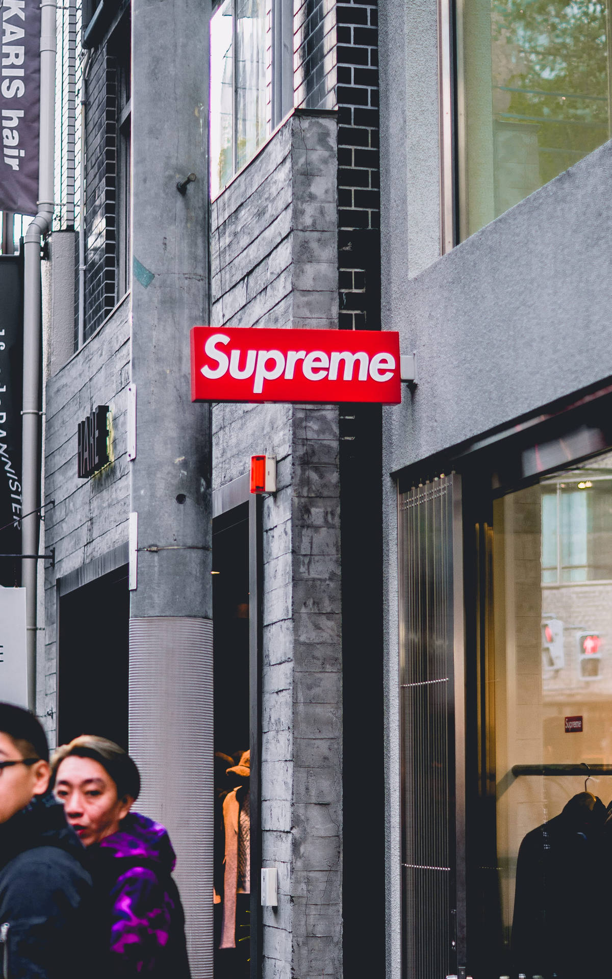 灰色磚建築上的紅色Supreme商店標誌，有行人走過。