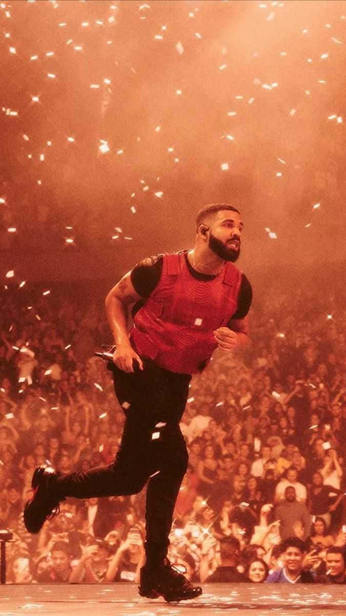 Drake 桌布 壁紙 — Drake 充滿活力地在舞台上奔跑，五彩紙屑如雨般灑落在被溫暖橙色燈光籠罩的喧鬧人群上。