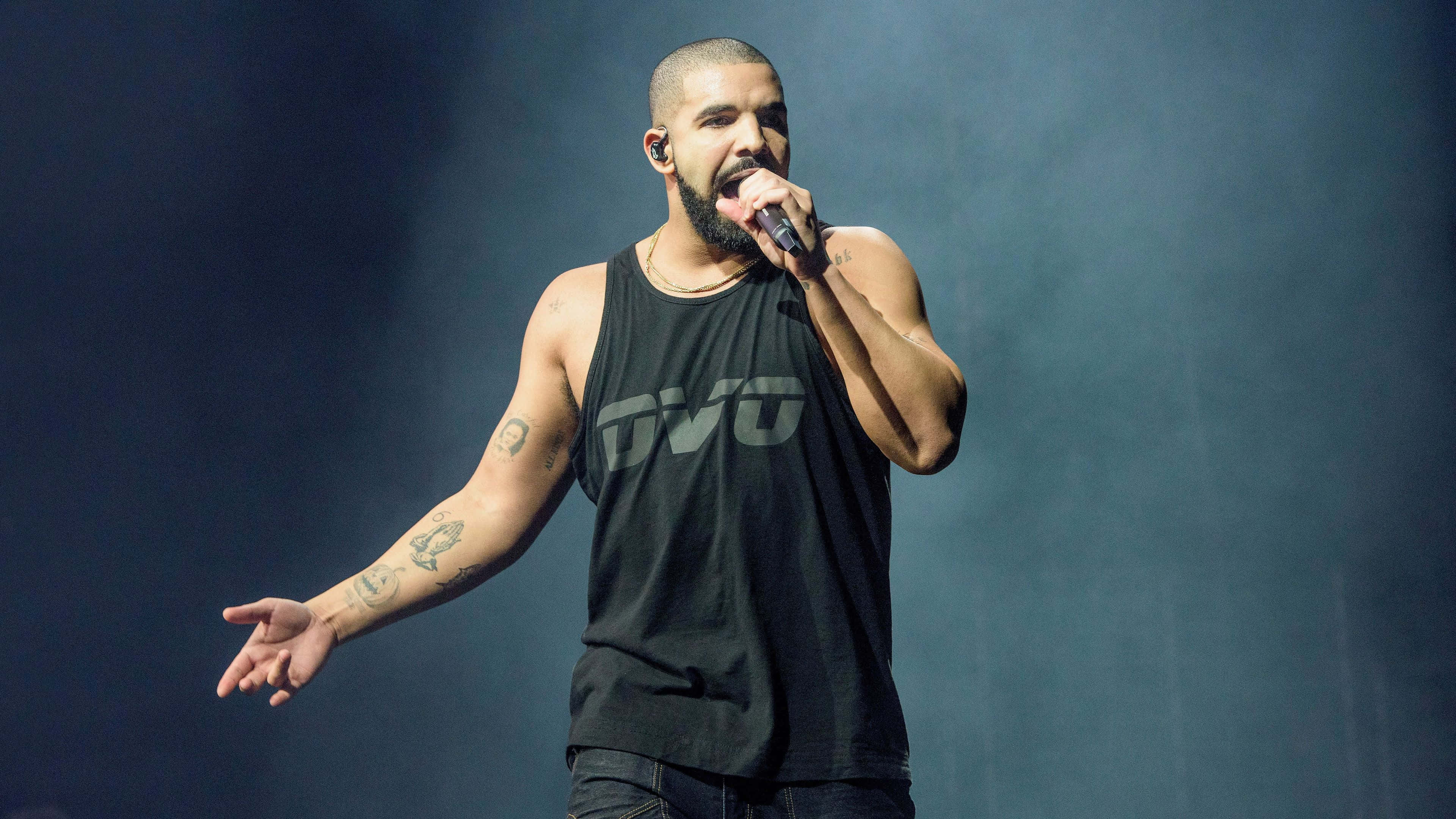 Drake 桌布 壁紙 — Drake 喺舞台上身穿黑色背心，喺戲劇性嘅藍色舞台燈光下揸住咪高峰表演。