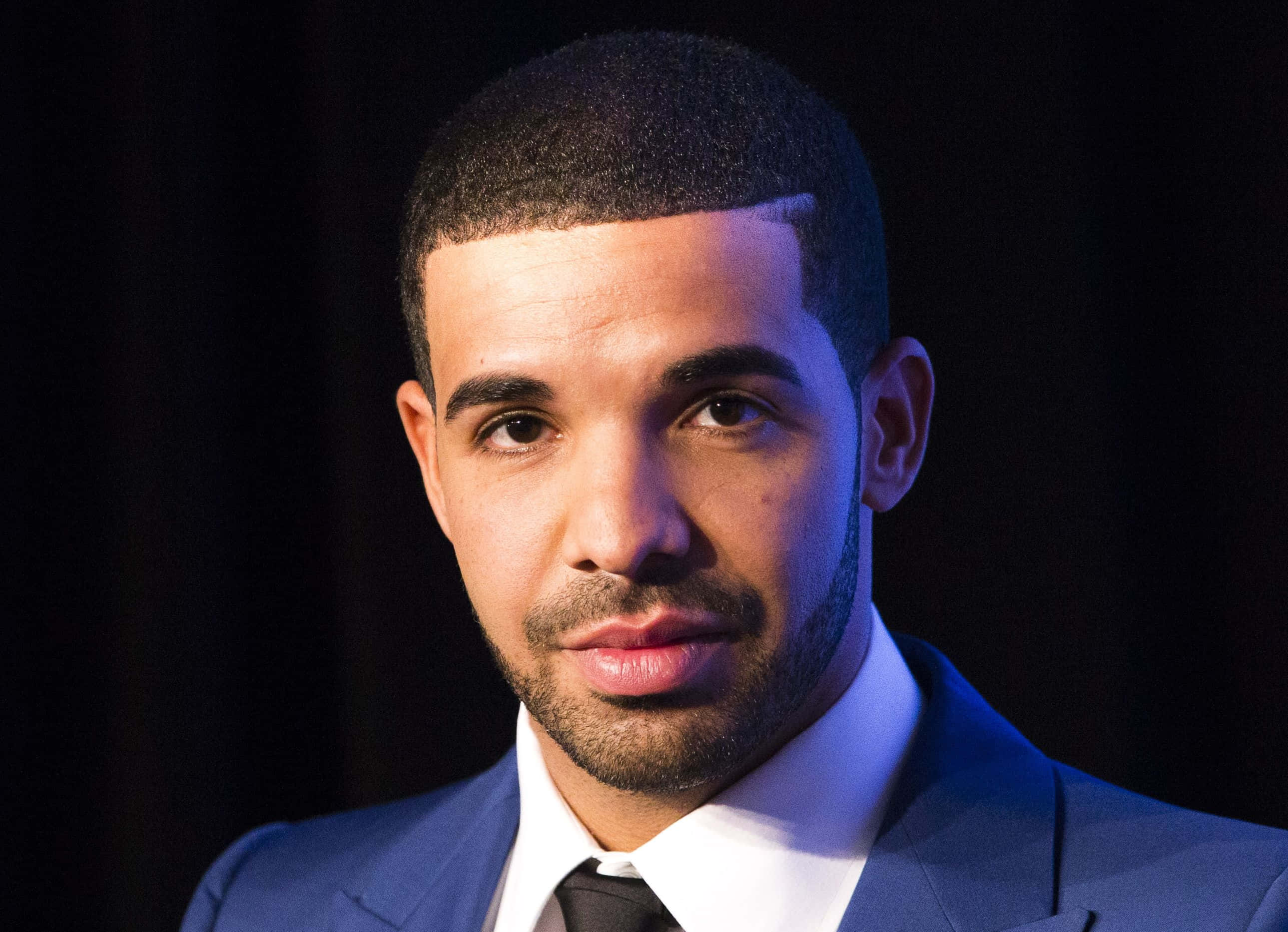 Drake 桌布 壁紙 — Drake 嘅特寫肖像，著住一套 sharp 藍色西裝，喺黑暗背景前配合戲劇性燈光。
