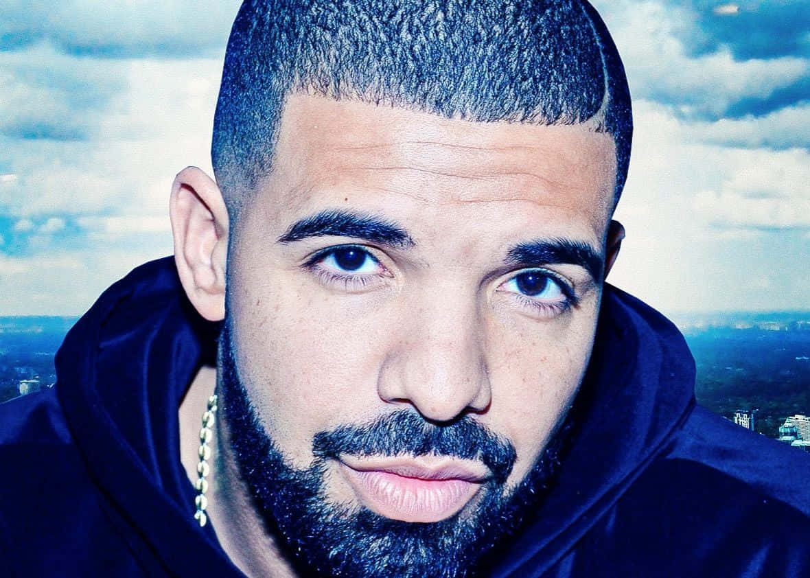 Drake 桌布 壁紙 — Drake 嘅特寫肖像，表情嚴肅，背景係多雲嘅天空同遠處嘅城市景觀。