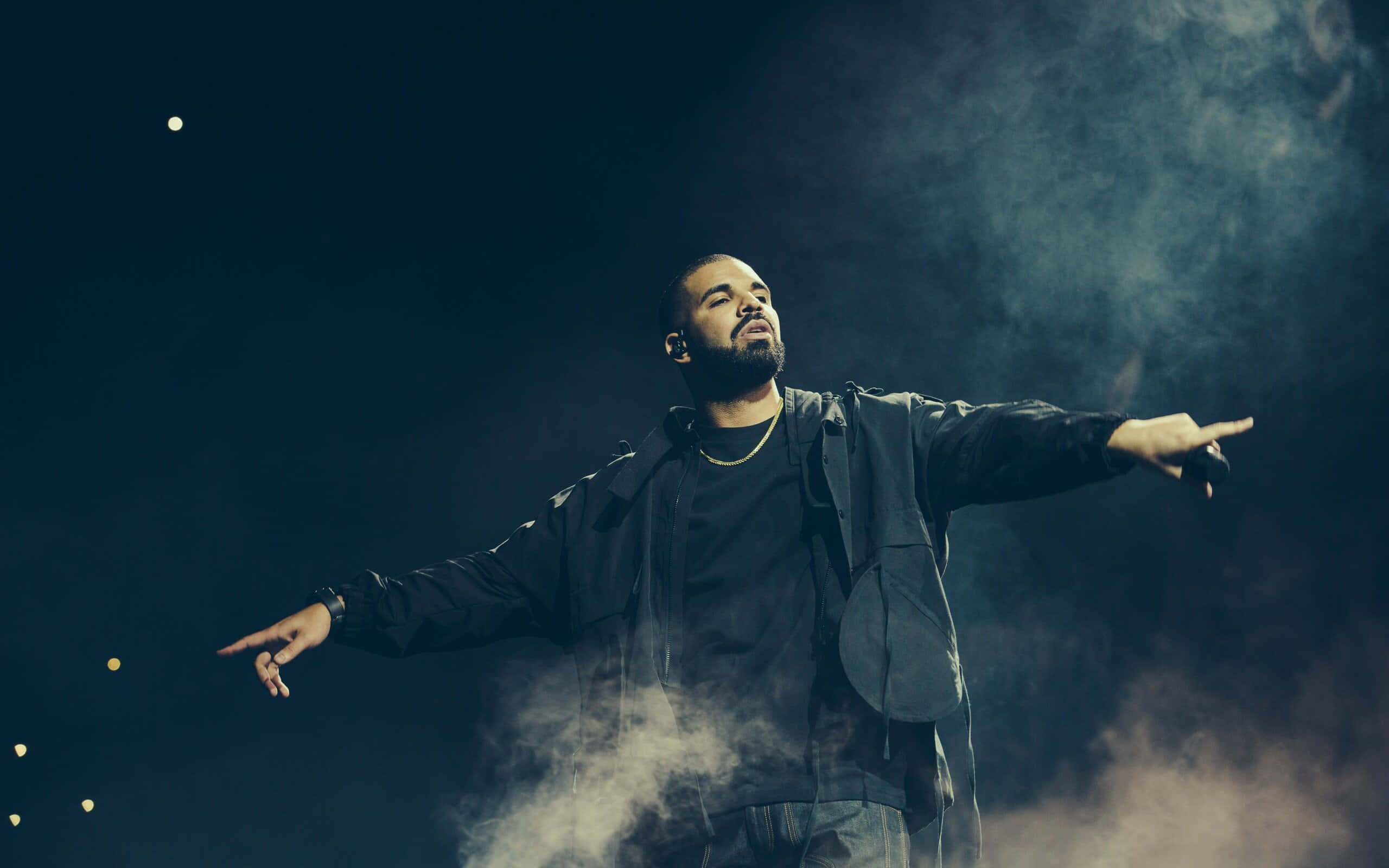 Drake 桌布 壁紙 — Drake 在夜晚煙霧彌漫的舞台上，在戲劇性燈光下張開雙臂表演。