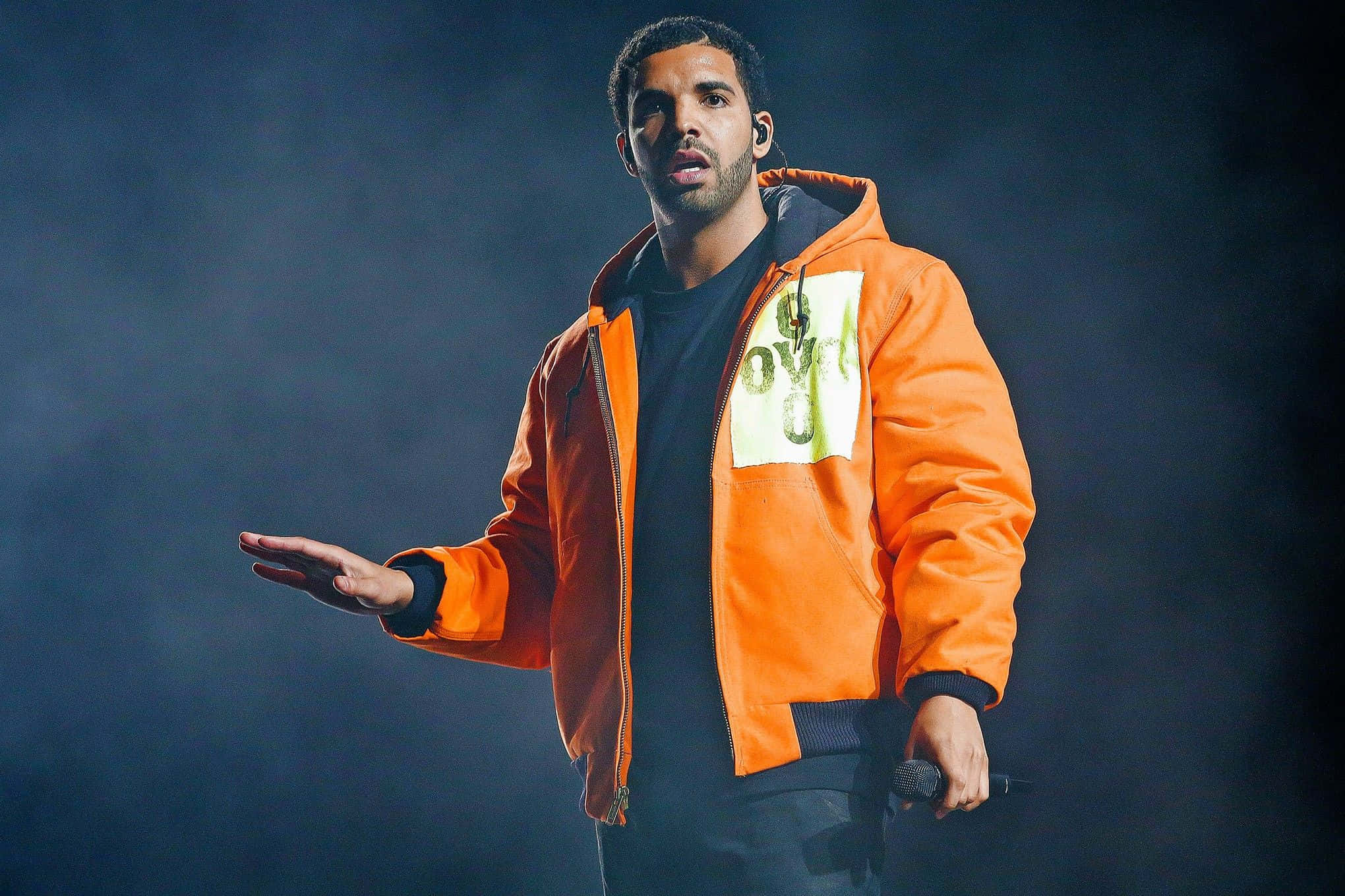 Drake 桌布 壁紙 — Drake 在煙霧瀰漫的黑暗背景下，穿著亮橙色外套在舞台上表演。